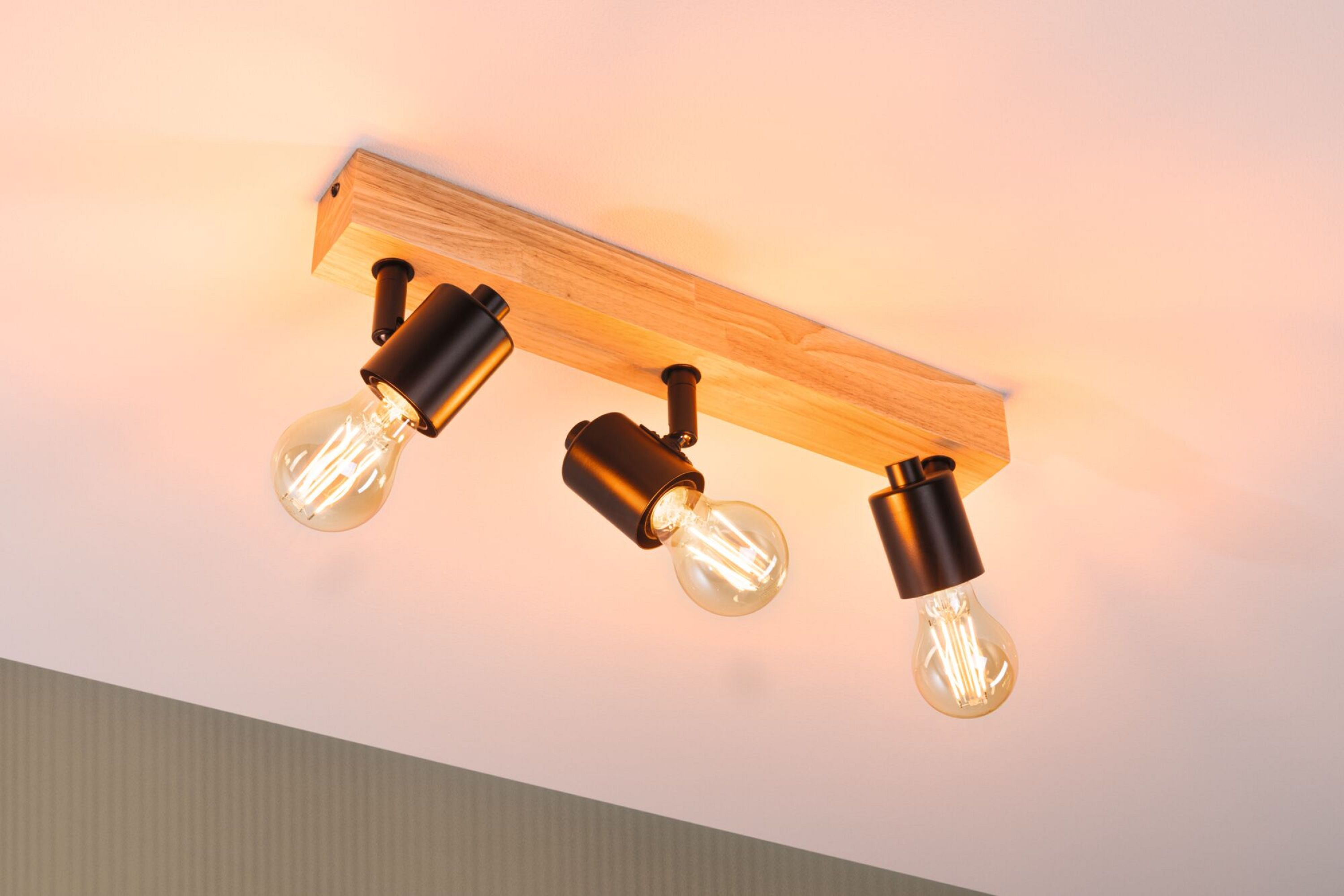 Lampa sufitowa z trzema czarnymi reflektorami i żarówkami Edisona, zamontowana na drewnianej belce.