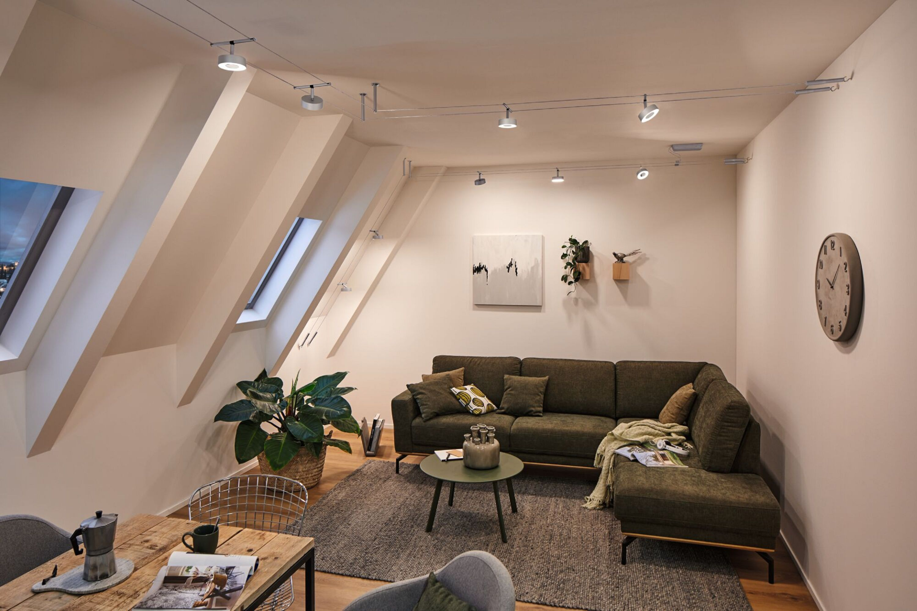Ein modernes Wohnzimmer mit grünem Sofa, Holztisch, Pflanzen und einer Uhr an der Wand.