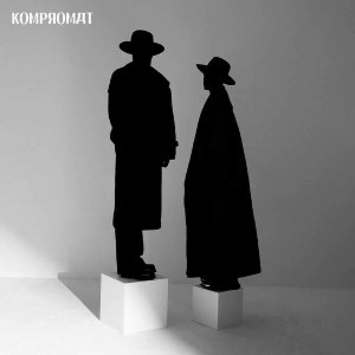 Due figure silhouettate con cappelli e lunghi cappotti su blocchi bianchi su sfondo bianco. La parola 'компромат' in alto.