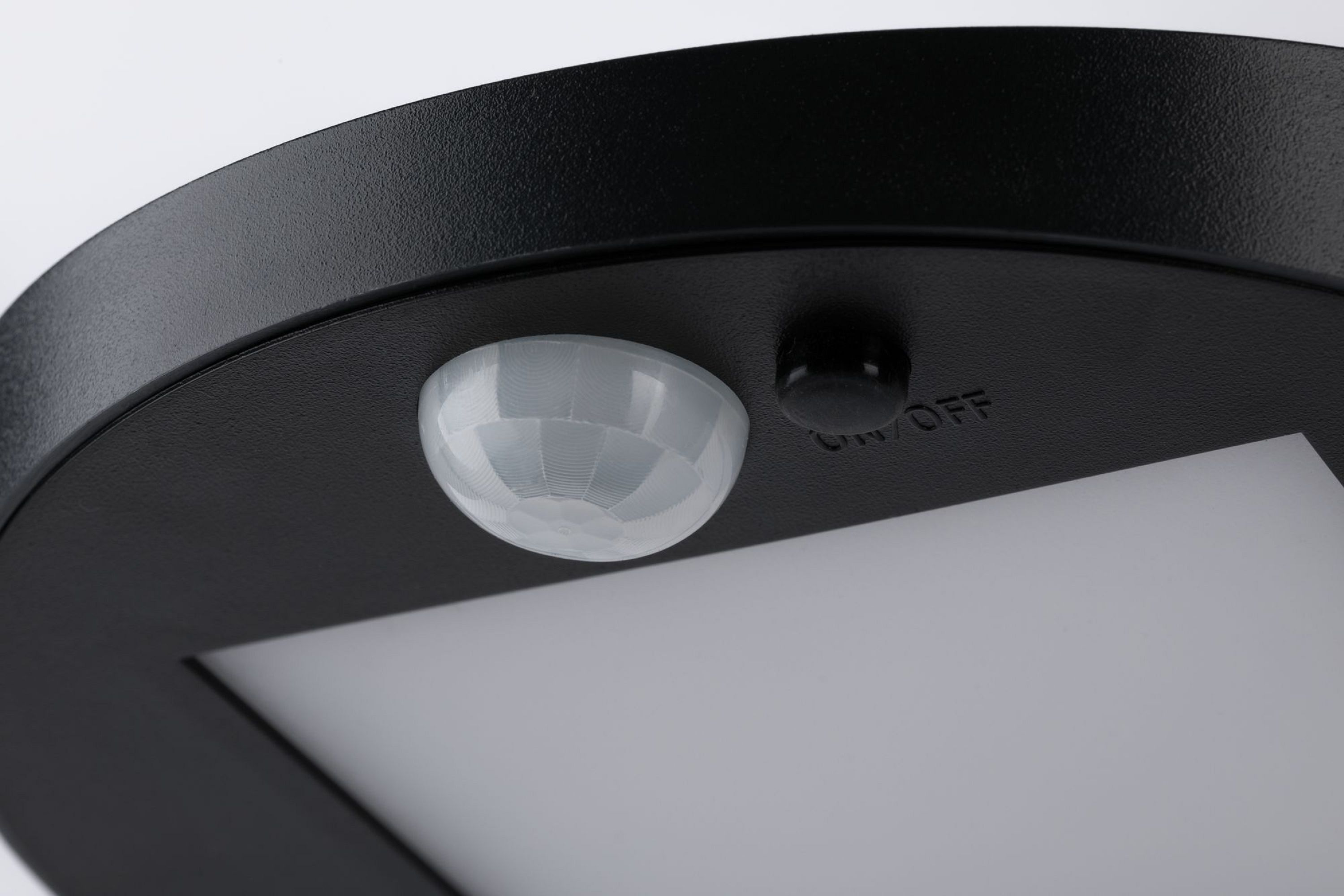 Zbliżenie czarnego, okrągłego urządzenia. Posiada czujnik, przycisk ON/OFF i biały panel świetlny.