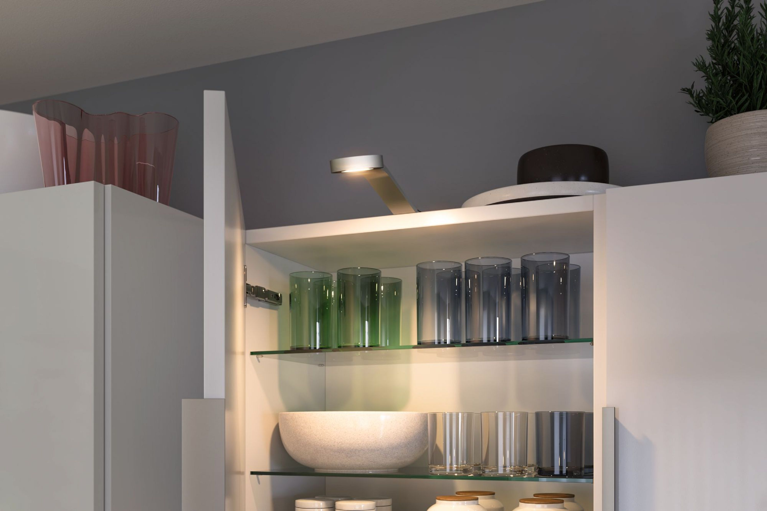 Offener Schrank mit Gläsern, einer Schüssel und einem Licht. Oben auf dem Schrank befinden sich eine Pflanze und Dekorationsartikel.