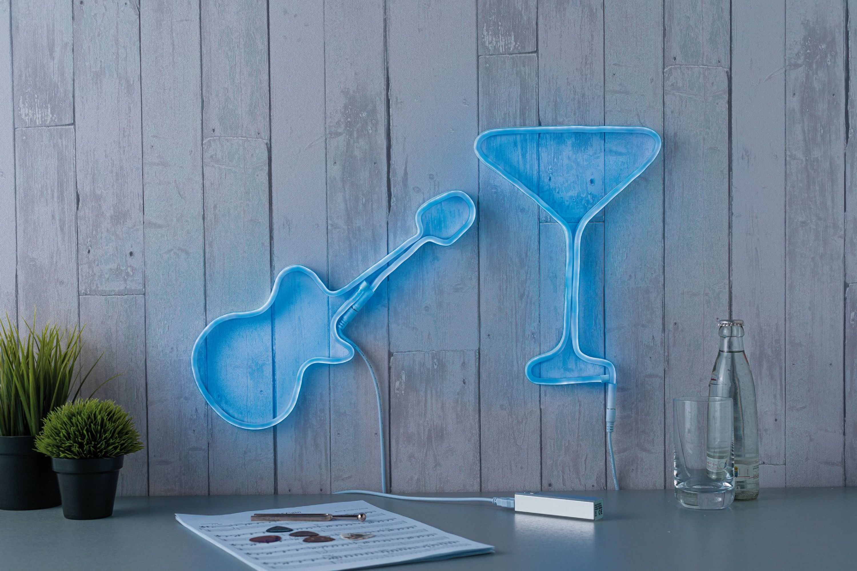 Niebieska neonowa gitara i kieliszek do martini na drewnianej ścianie. Nuty i szklanka na stole.