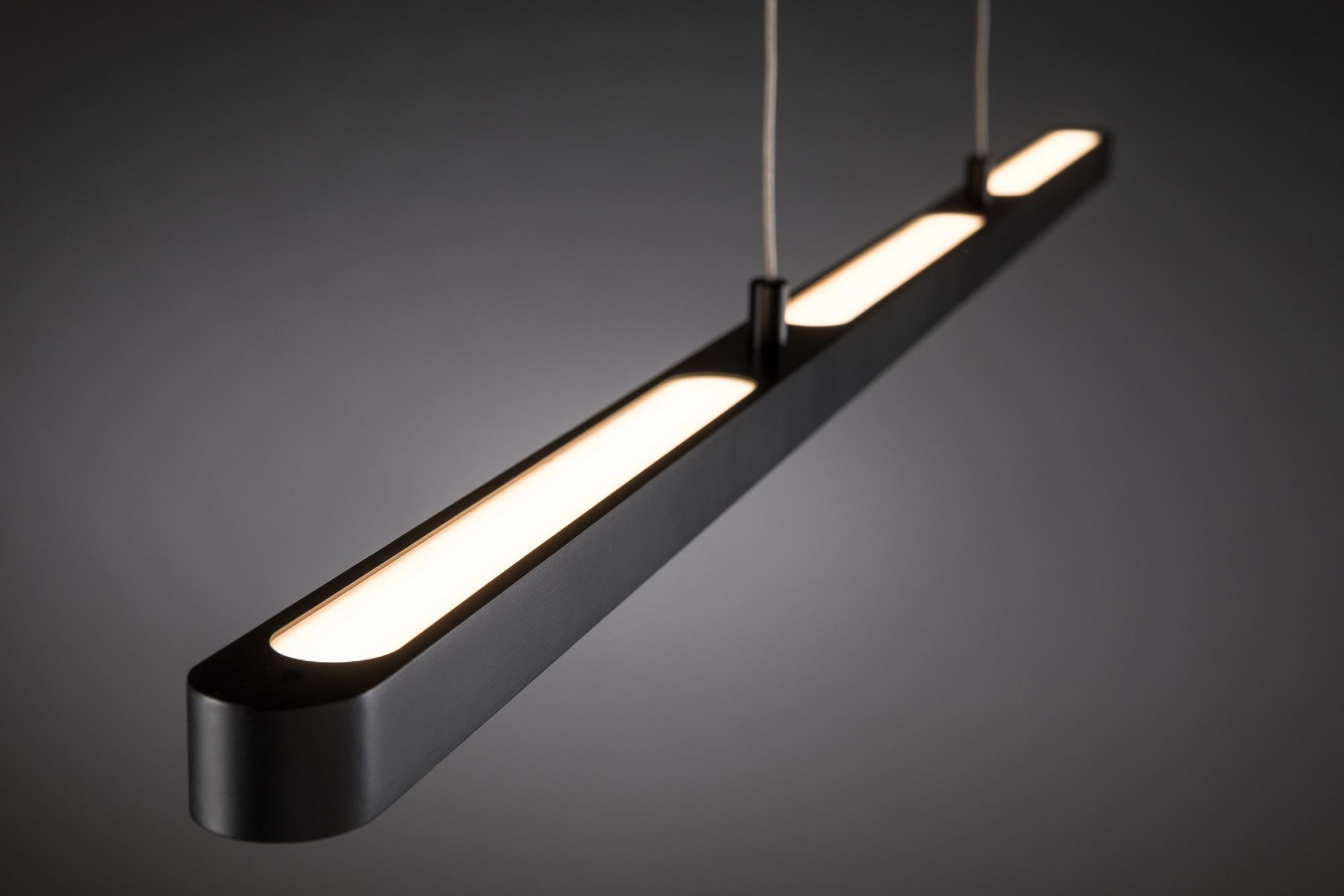 Eine schwarze, rechteckige Leuchte hängt von der Decke. Es hat einen beleuchteten weißen Lichtstreifen.