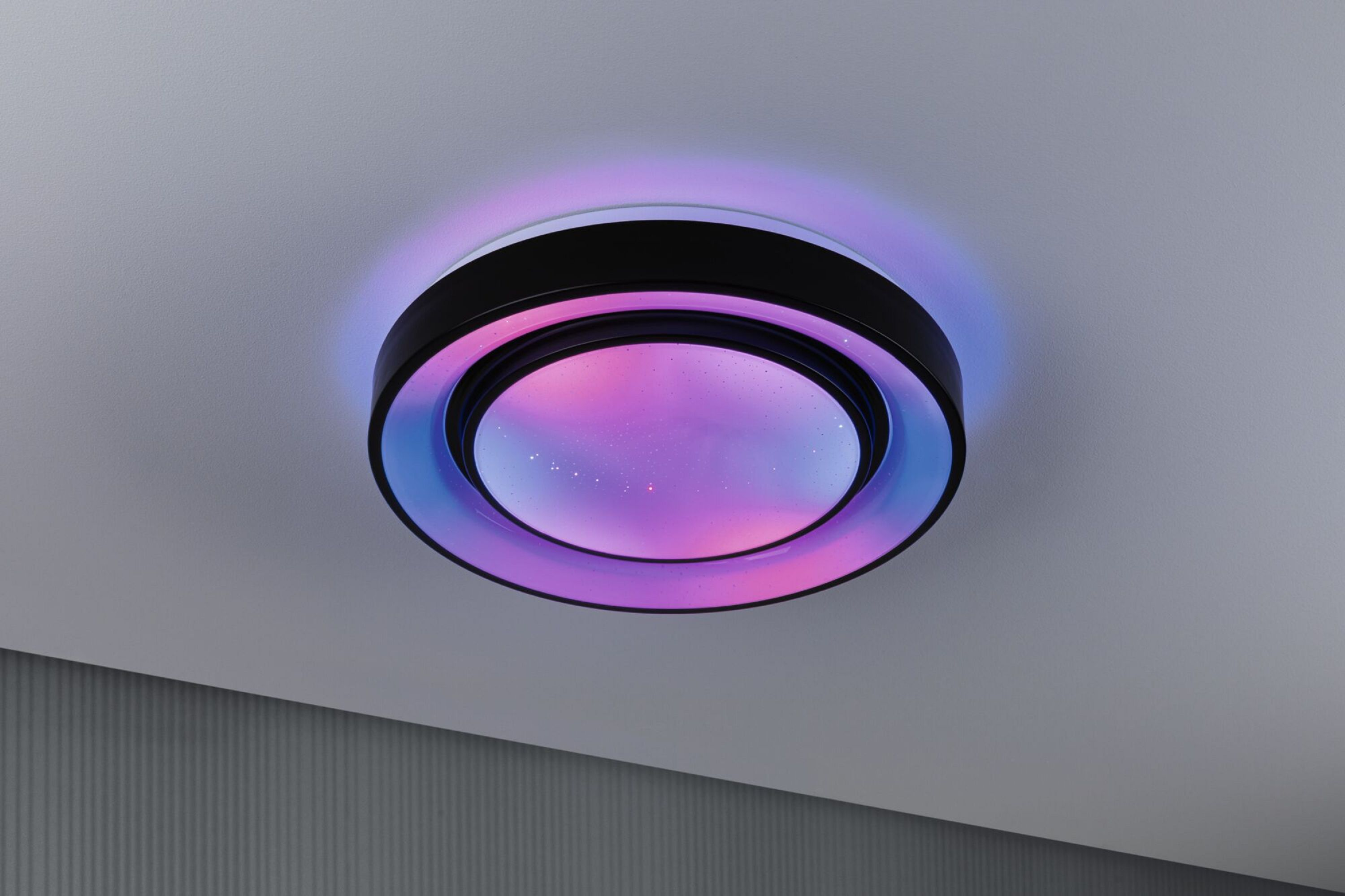 Un plafonnier avec une bordure noire et des lumières changeant de couleur. Des teintes roses et bleues illuminent l'intérieur.