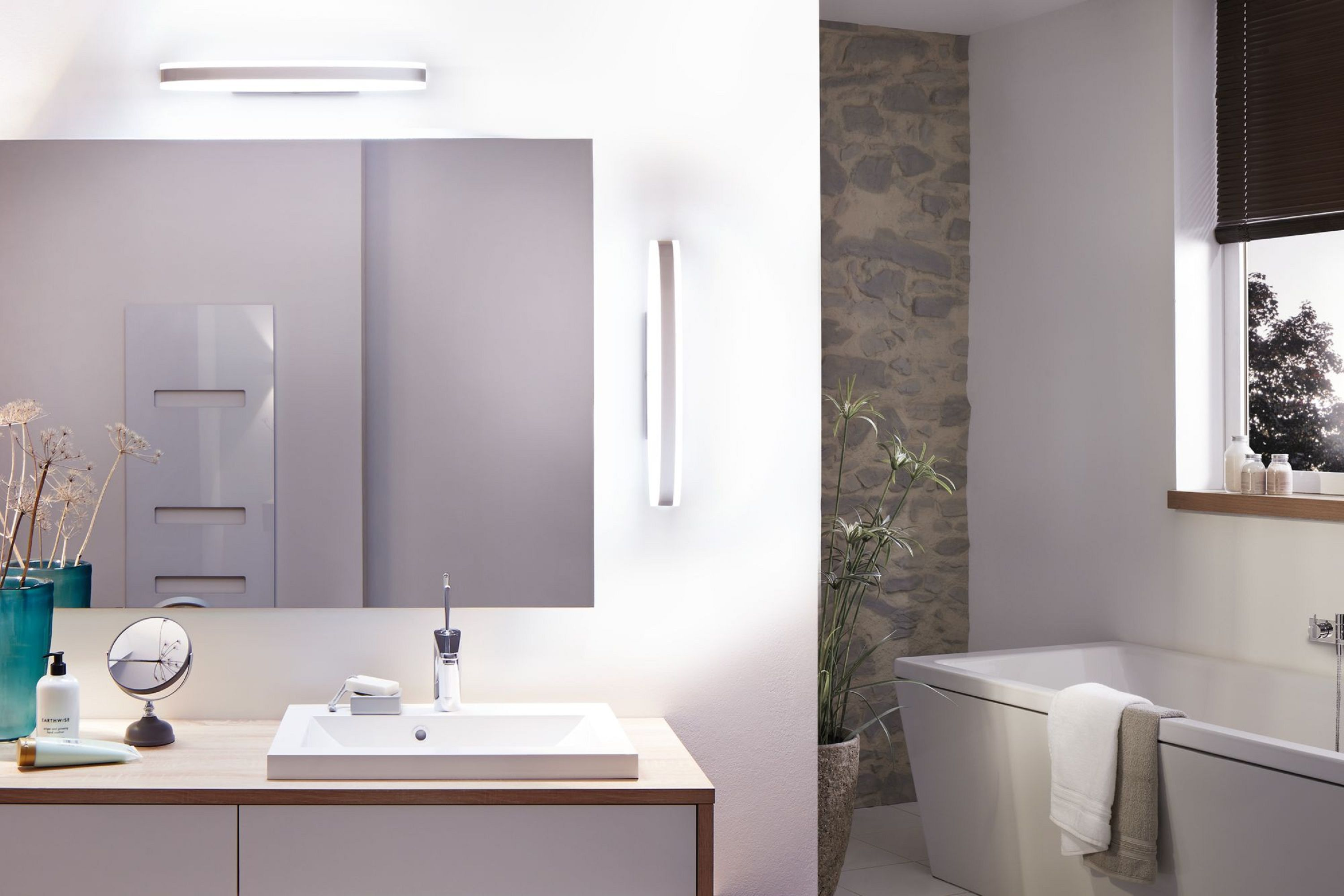 Modernes Badezimmer mit Spiegel, Waschbecken, Badewanne und Steinmauer. Enthält Pflanzen, ein Fenster und eine Leuchte.