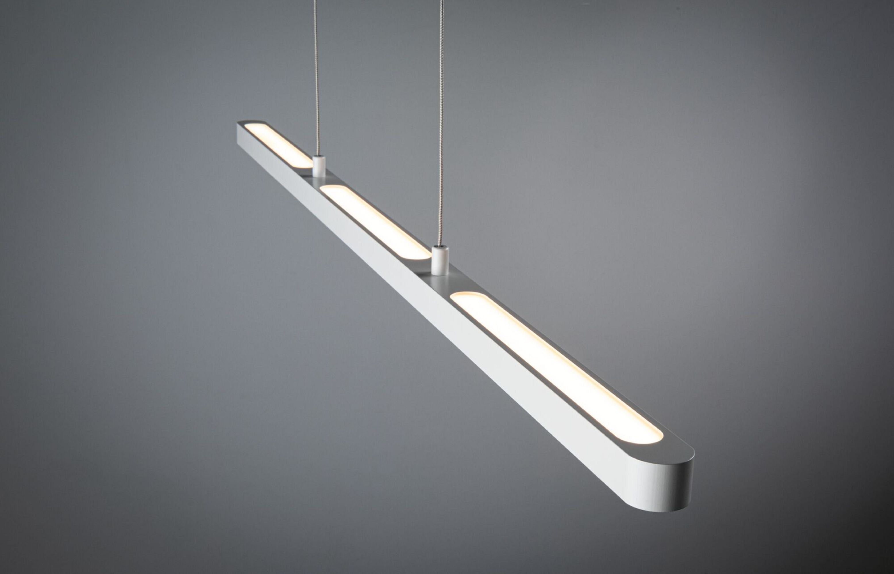 Un'elegante lampada a LED bianca è sospesa a fili sottili su uno sfondo grigio. Ha tre sezioni illuminate.