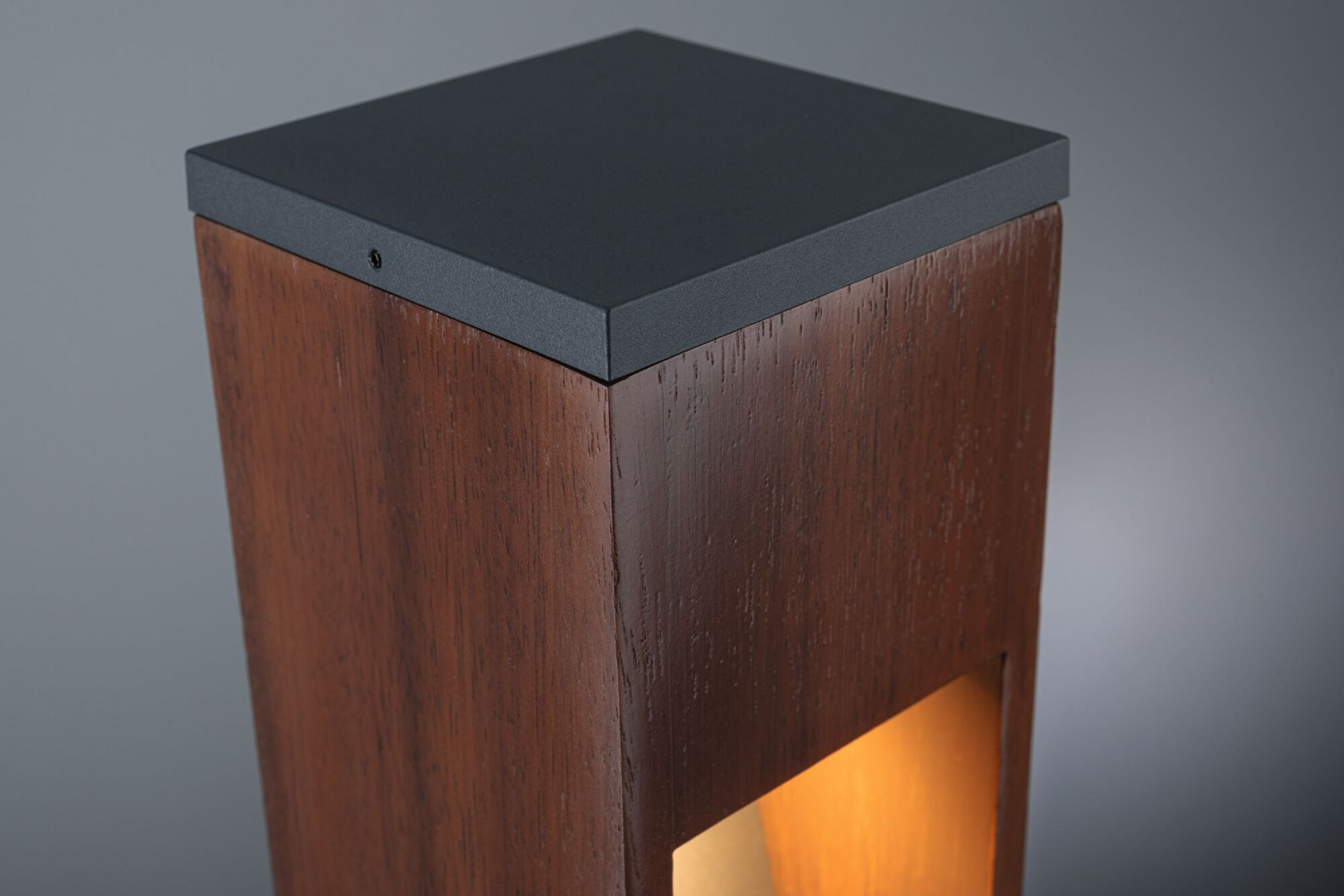 Drewniana prostokątna lampa z czarnym blatem. Ma ciepłe światło wydobywające się z prostokątnego otworu.