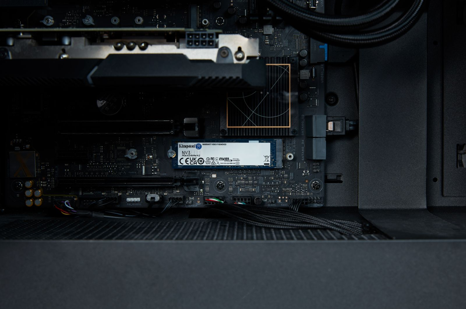 Wewnątrz obudowy komputera. Dysk SSD Kingston NV3 jest zainstalowany na płycie głównej. Widoczne są kable i inne elementy.