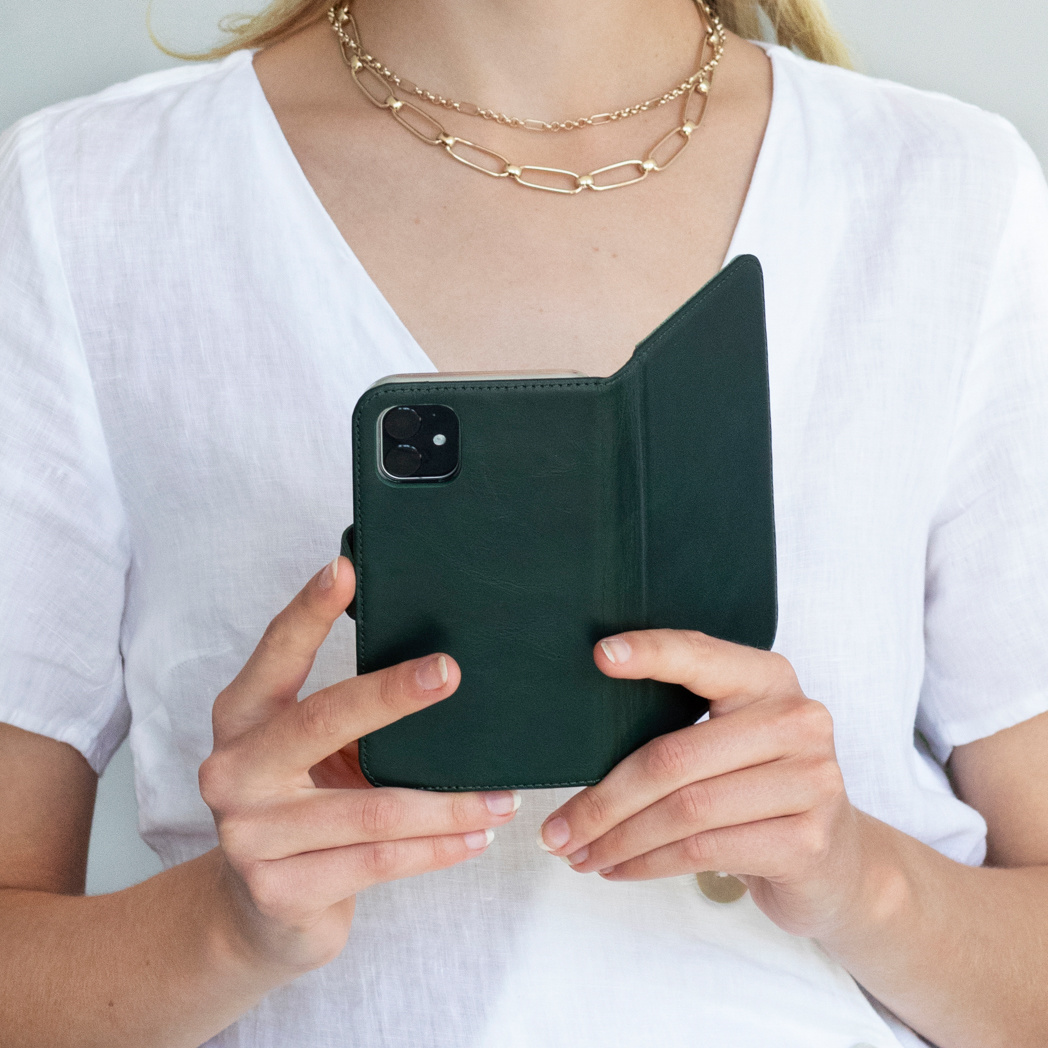 Een vrouw houdt een donkergroene telefoonhoes vast. Ze draagt een wit overhemd en een gouden ketting. De achtergrond is effen.