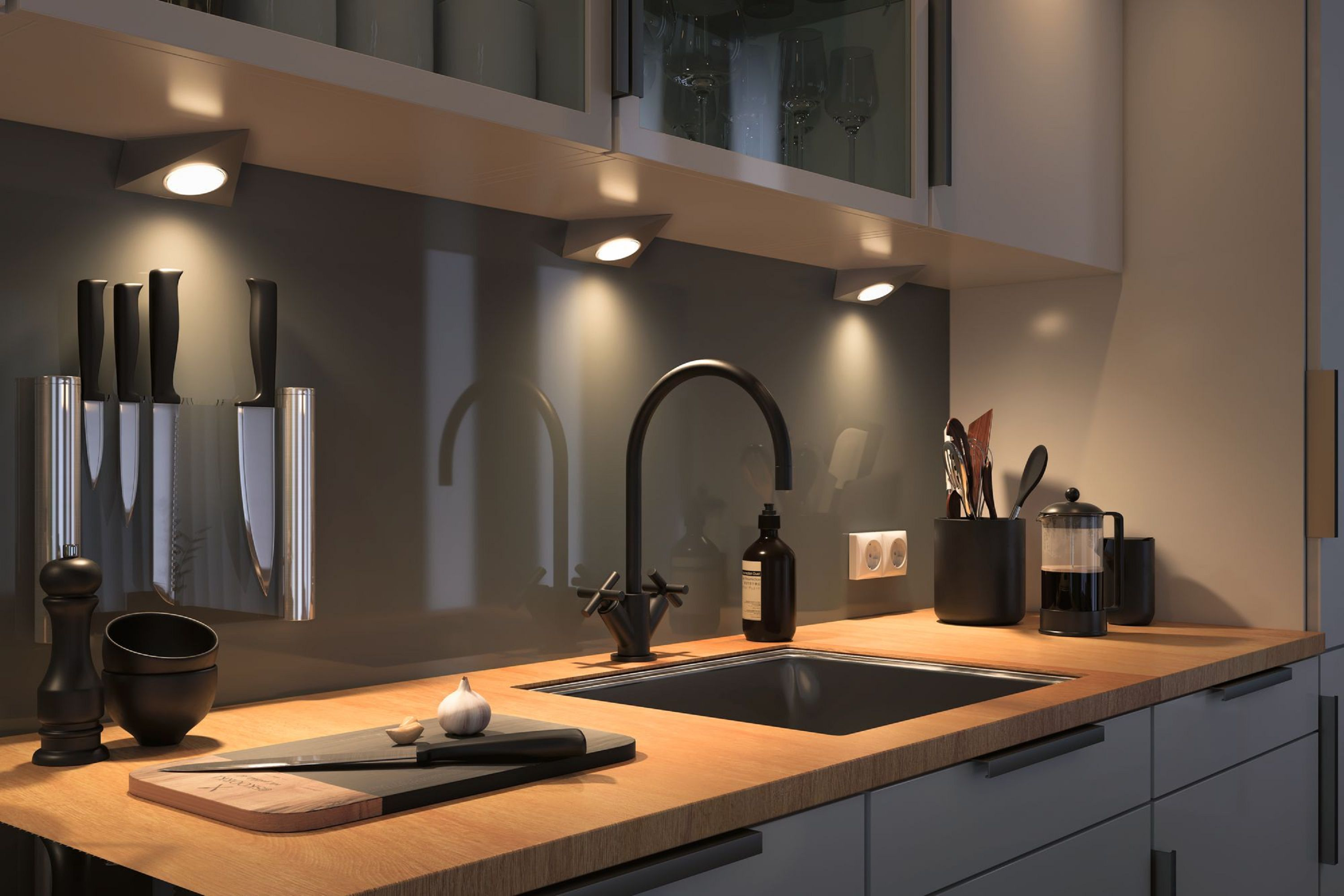 Interni cucina con coltelli, lavandino e tagliere. Le luci brillano sul piano di lavoro in legno.