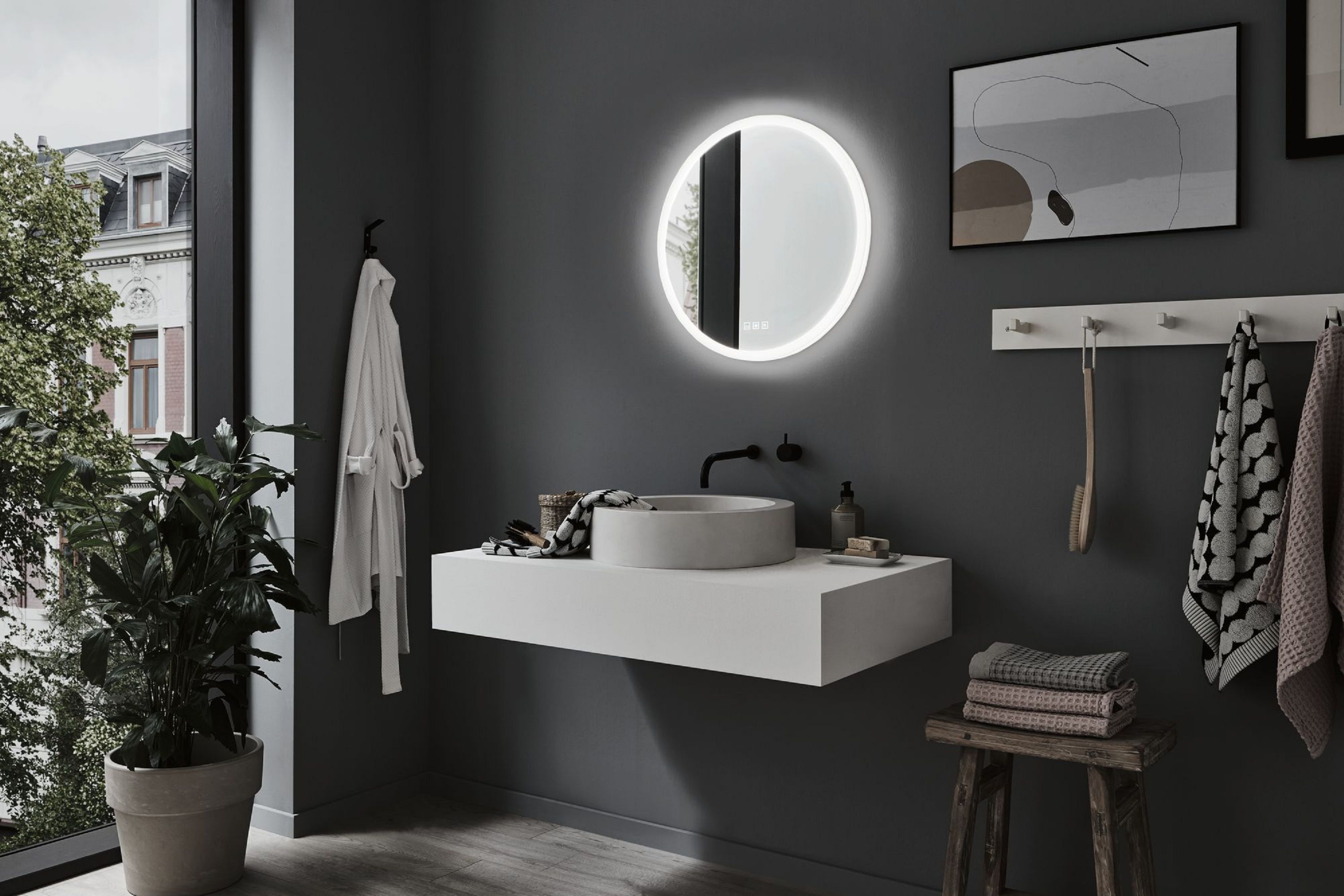 Salle de bain moderne avec miroir rond, lavabo flottant, serviettes et plante en pot. Le mur est gris.