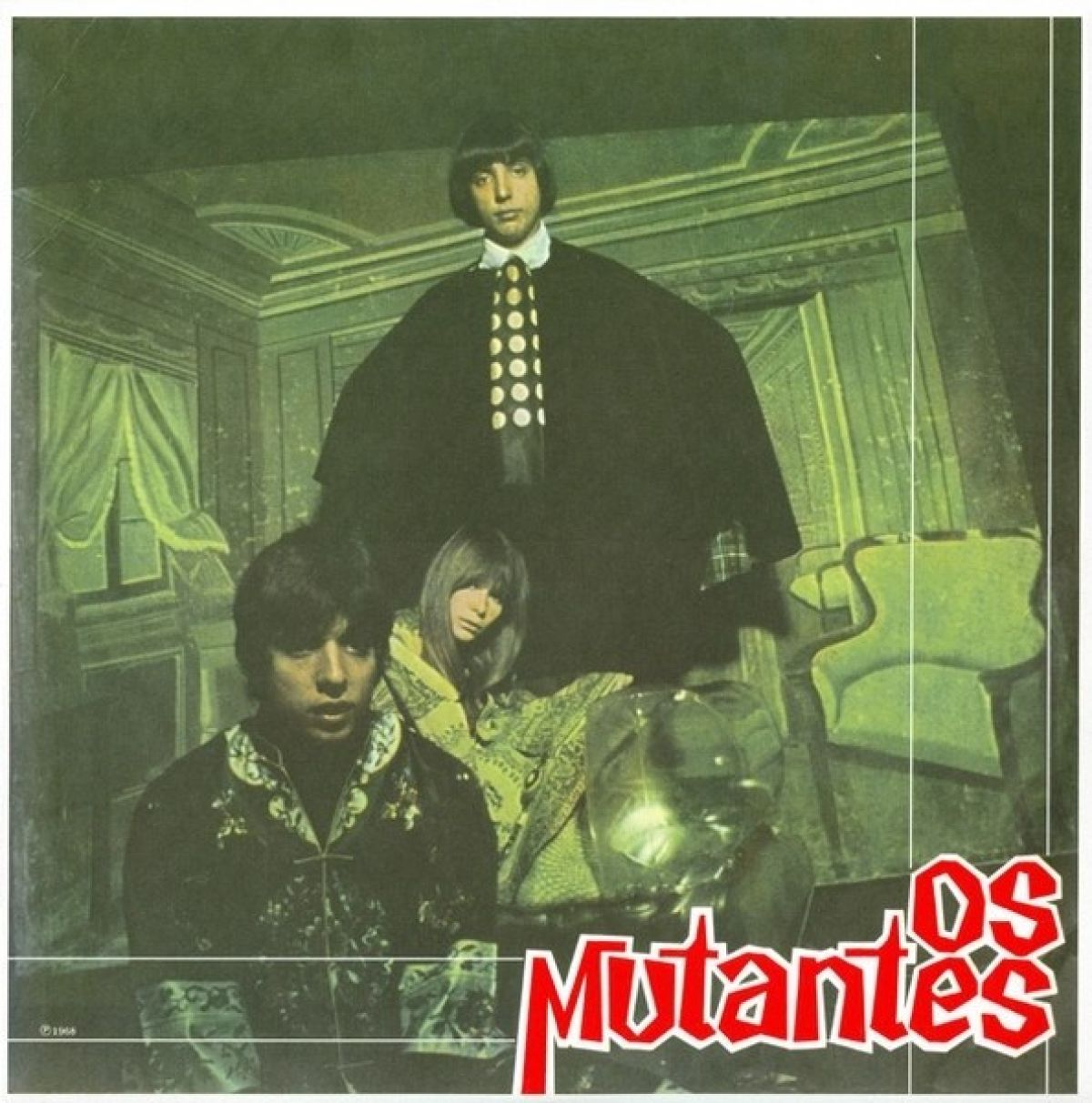 Una copertina di un album vintage presenta quattro membri della band. Il nome della band è in rosso e bianco. Lo sfondo è una vecchia stanza, con toni verdi.