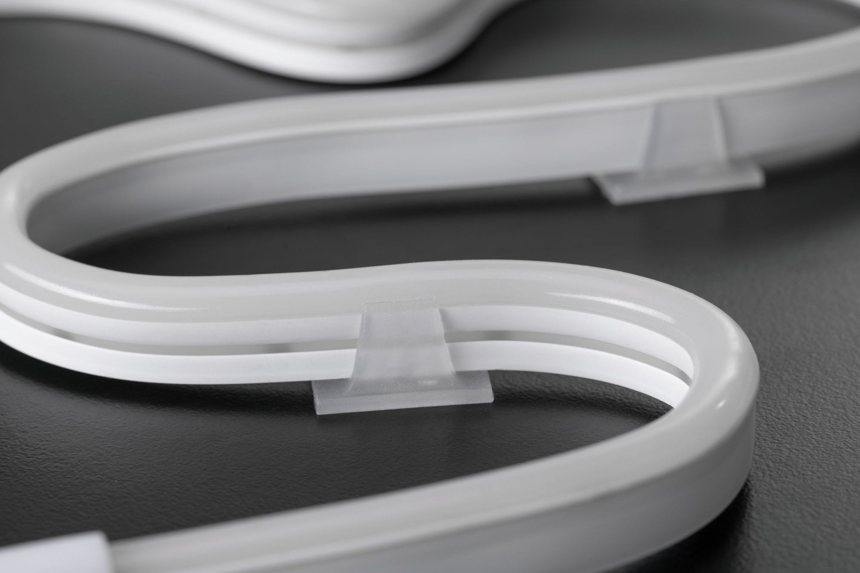 Zbliżenie białej, zakrzywionej, neonowej oprawy oświetleniowej z przezroczystymi klipsami na ciemnej powierzchni.