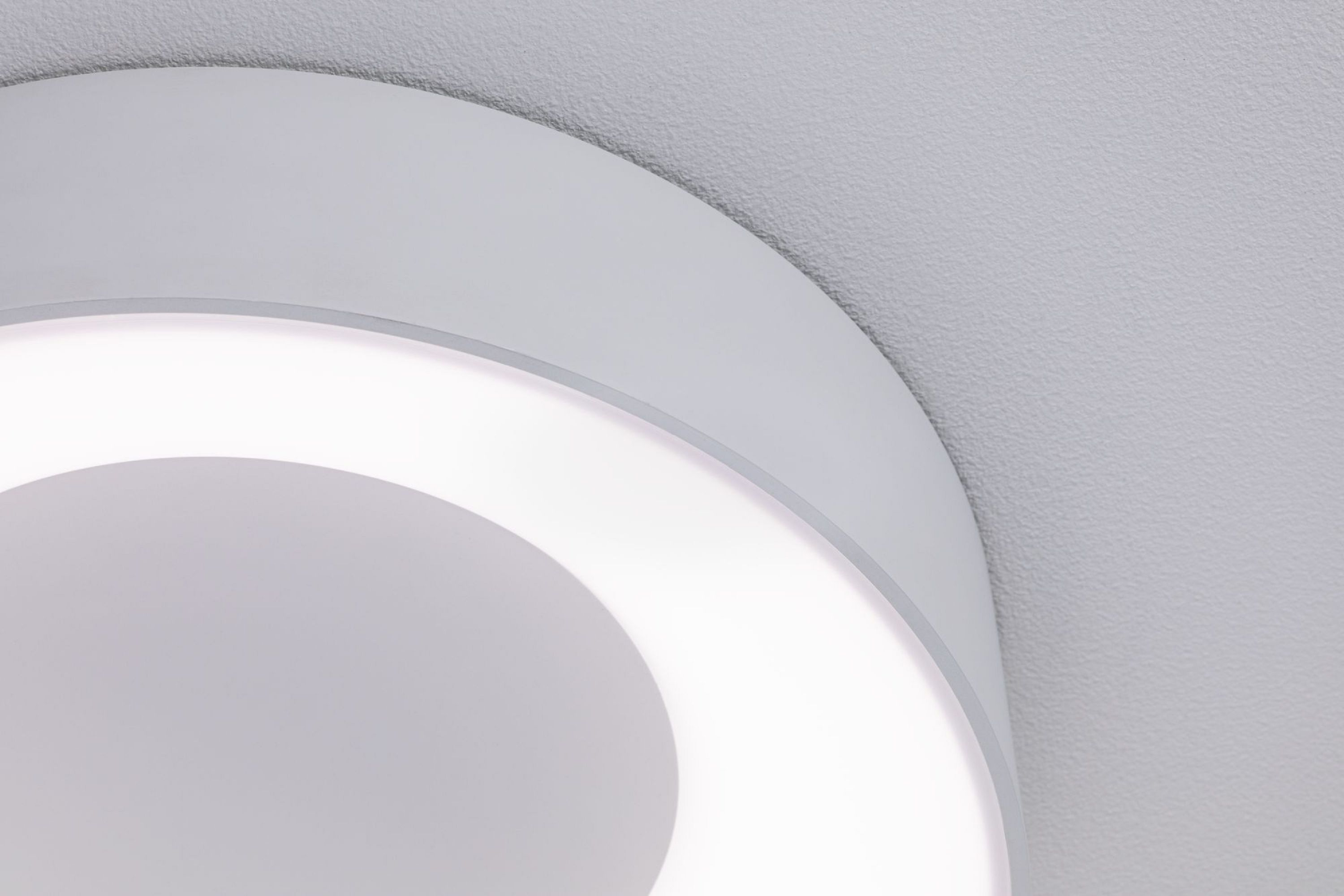 Primo piano di una plafoniera circolare bianca. La luce ha un anello interno luminoso, contro un soffitto bianco strutturato.