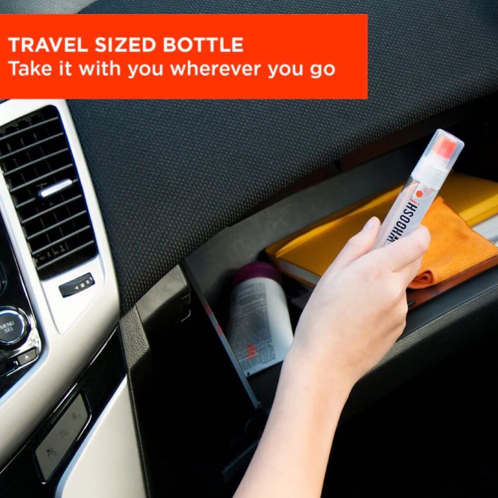 Eine Hand hält eine Reisegröße-Flasche im Handschuhfach eines Autos. Weitere Gegenstände sind ein Notizbuch, ein orangefarbenes Tuch und eine Flasche.