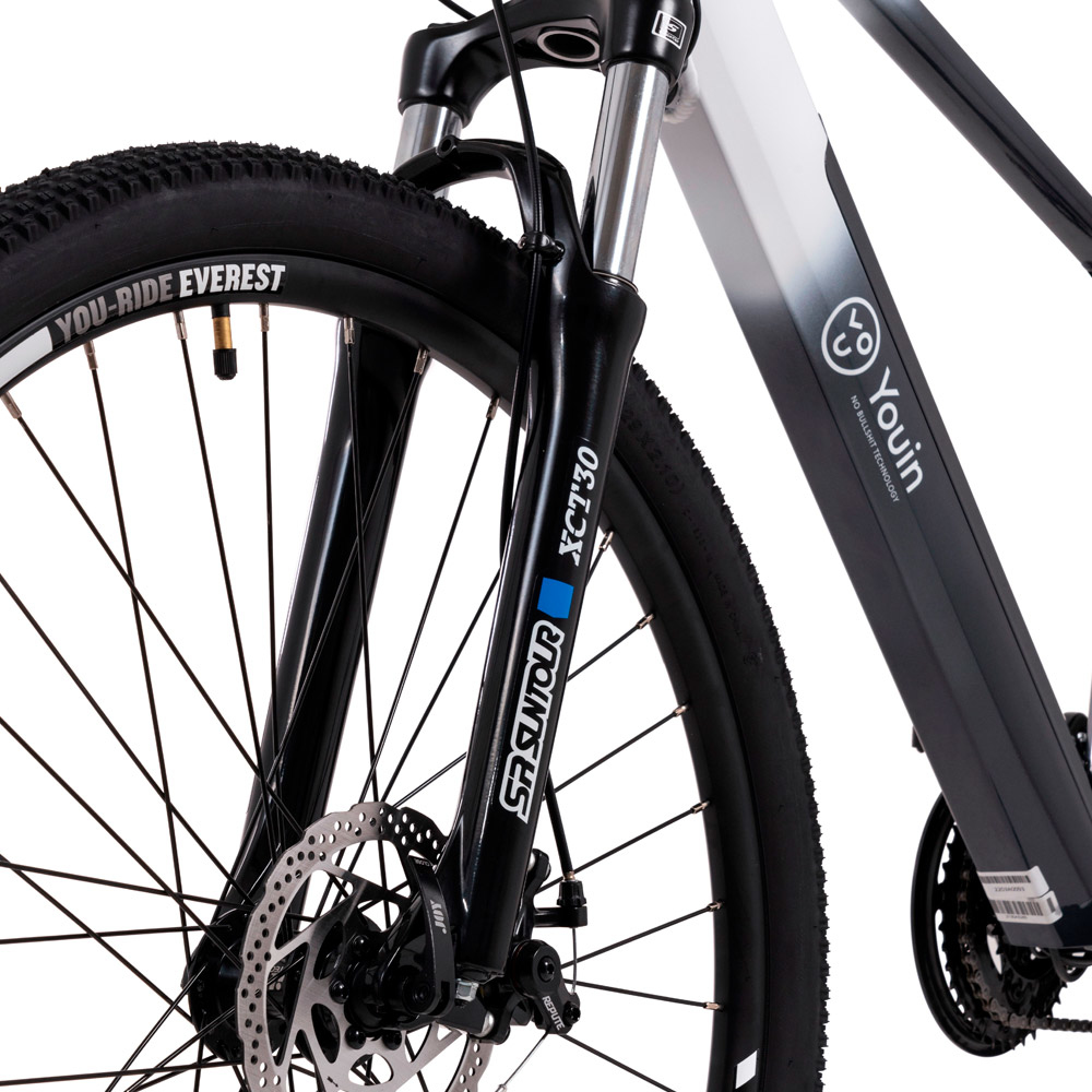 Nahaufnahme eines Fahrrad-Vorderrads. Schwarzer Reifen mit 'You-Ride Everest'. Schwarze Federung und Bremsscheibe sichtbar.