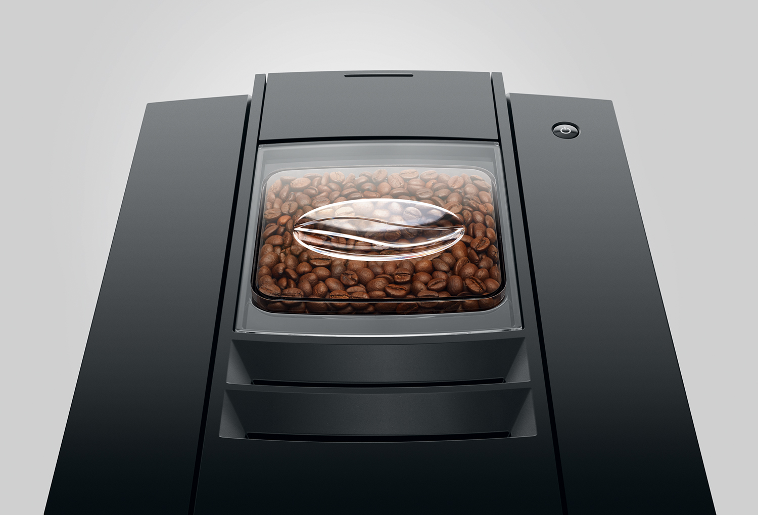 Primer plano de una cafetera negra con un recipiente transparente lleno de granos de café. Hay una forma de grano de café en el recipiente.