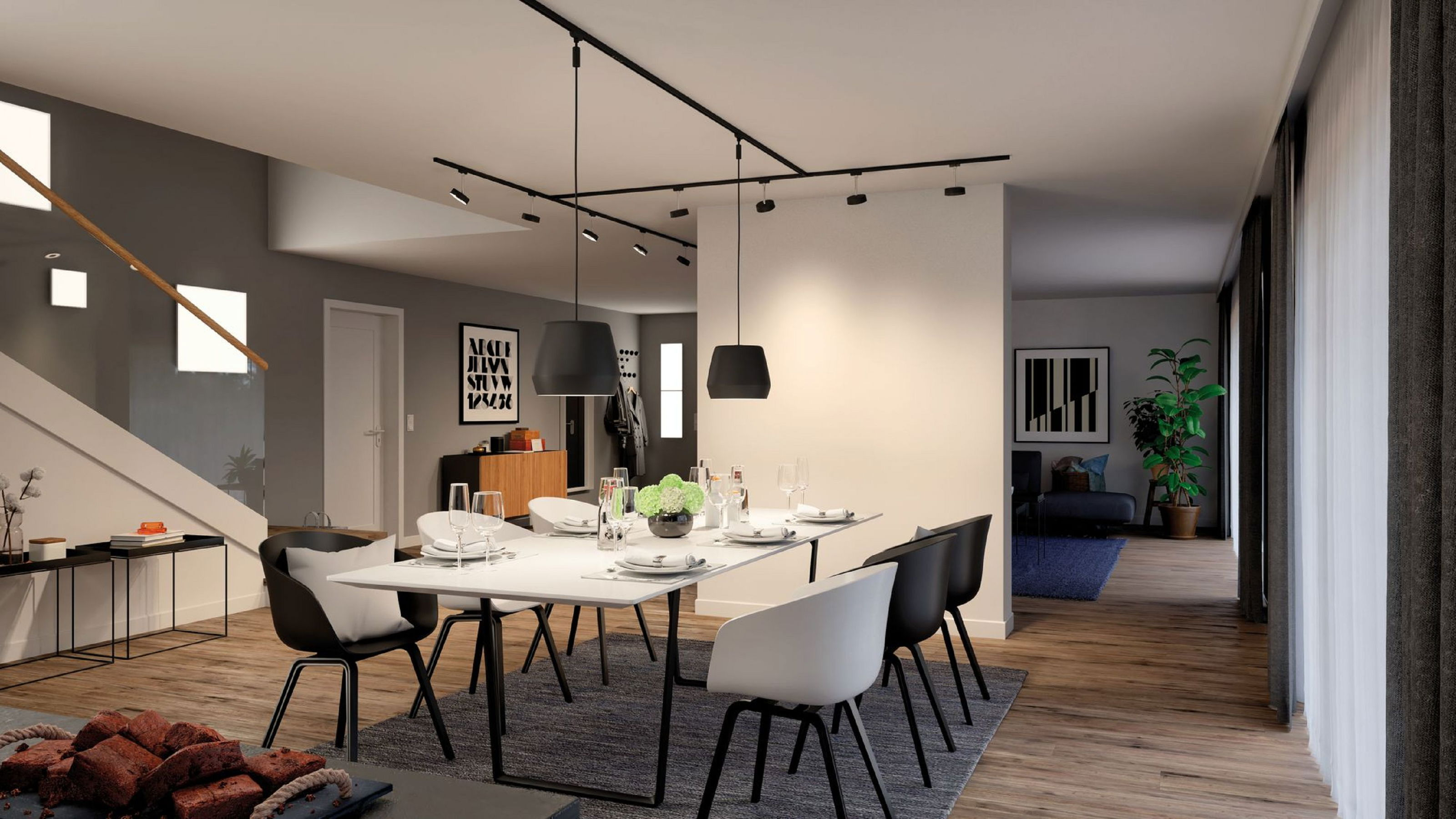 Ein modernes Esszimmer mit weißem Tisch, schwarzen Stühlen und Blick in ein anderes Zimmer mit Sofa und Pflanze.