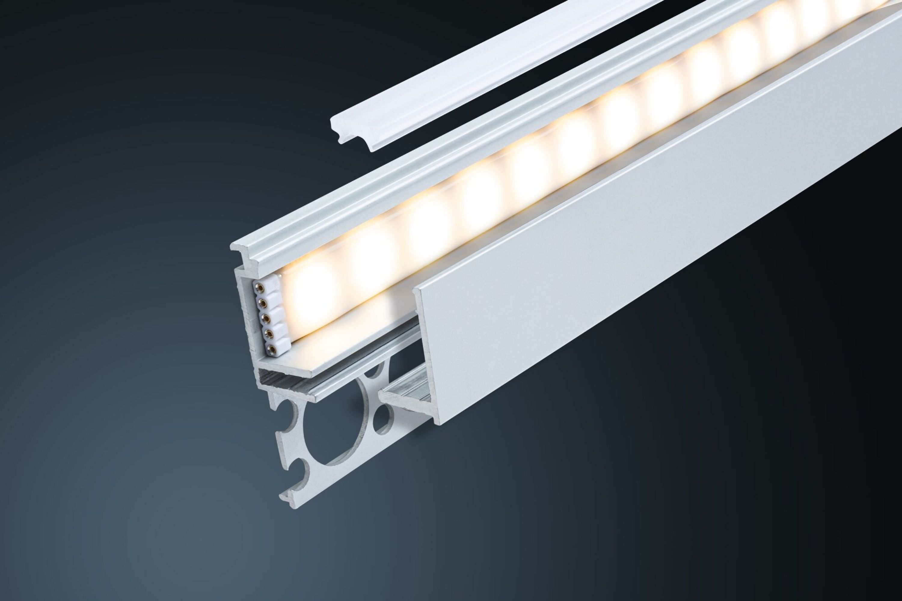 Eine LED-Leuchte aus Aluminium mit weißem Diffusor, die Innenlichter zeigt. Auf dunklem, grauem Hintergrund.