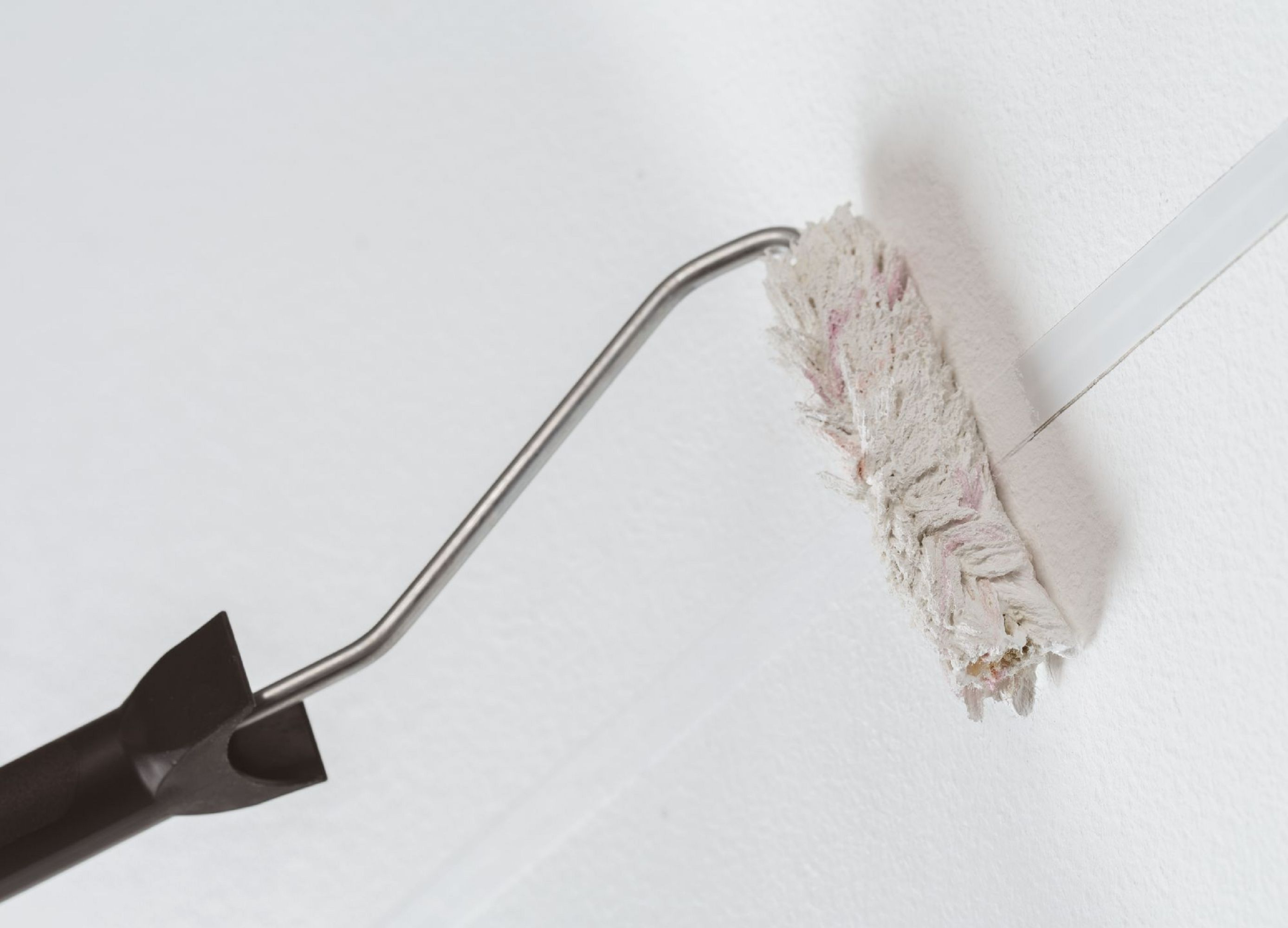 Eine Farbrolle trägt Farbe auf eine weiße Wand auf. Die Rolle ist beige mit einem Metallgriff und schwarzem Griff.