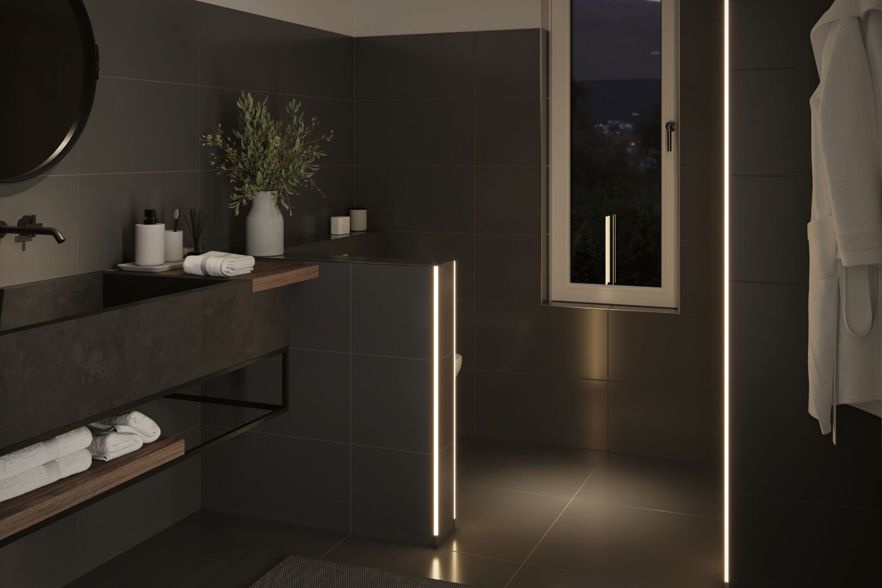 Modernes Badezimmer mit dunklen Fliesen, rundem Spiegel und Waschbecken. Es gibt ein Fenster und einen Bademantel. Sanfte Beleuchtung.