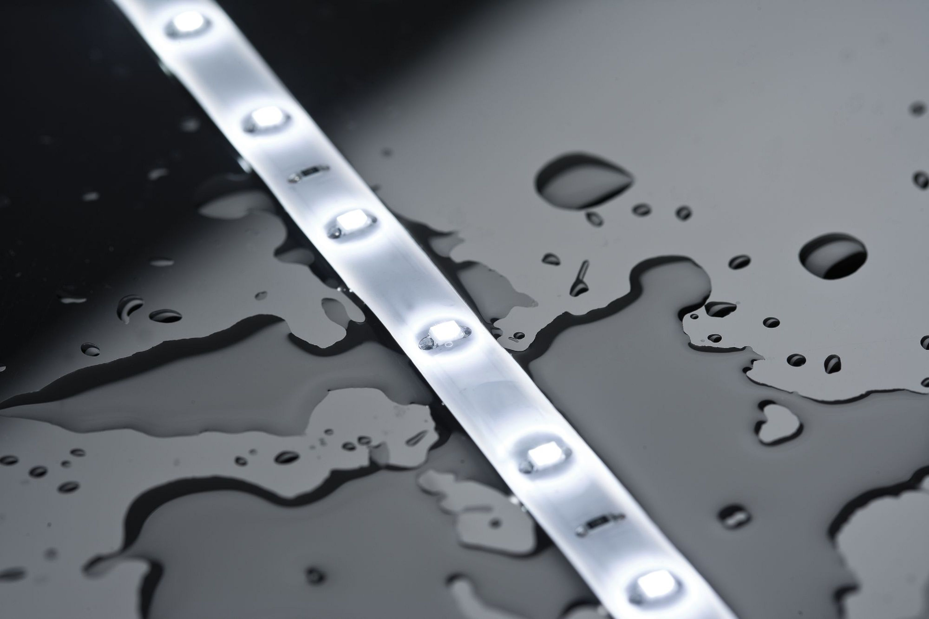 Ein beleuchteter LED-Streifen auf einer nassen, reflektierenden Oberfläche. Wassertropfen sind verstreut.