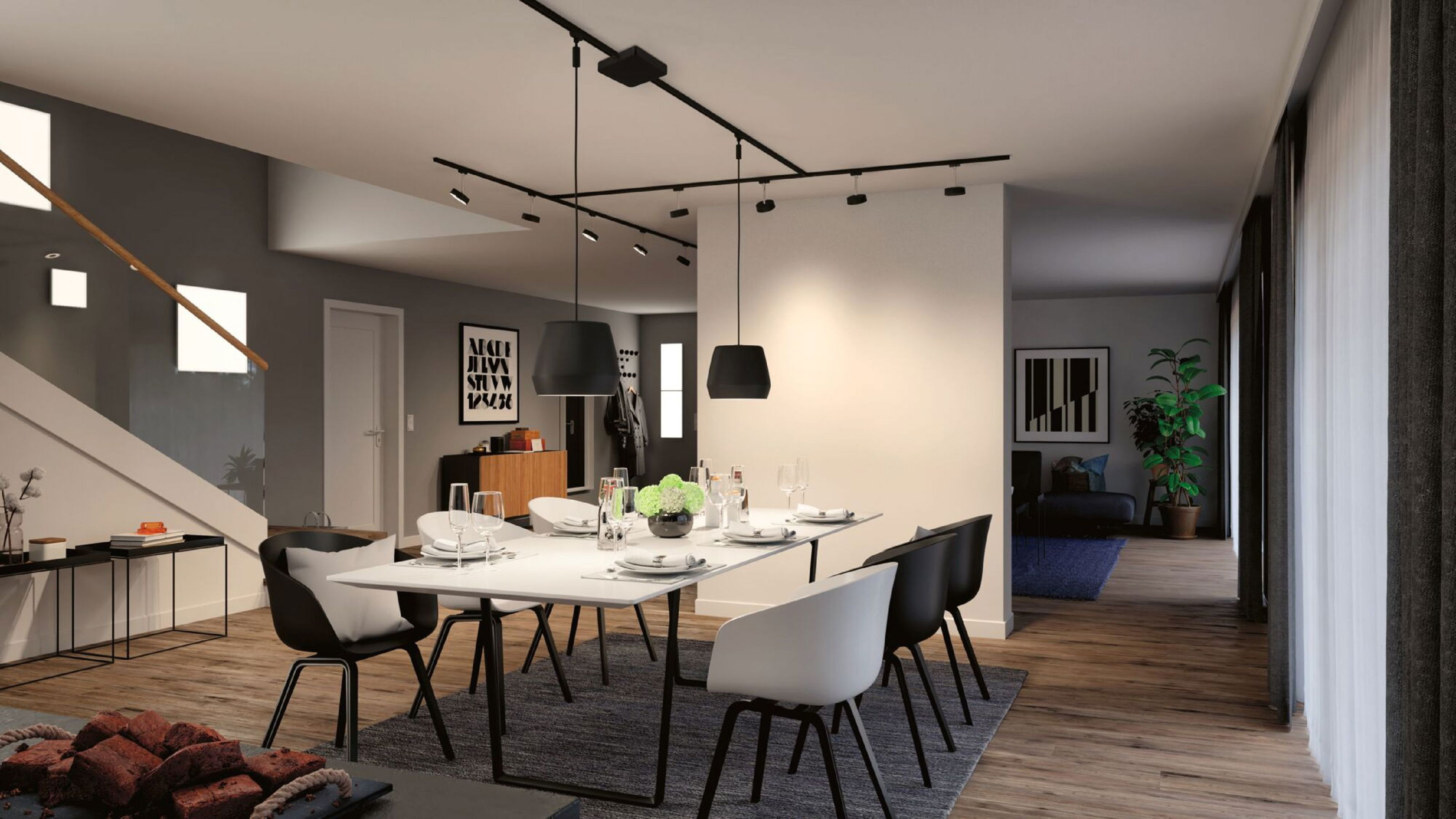 Esszimmer mit gedecktem Tisch, schwarzen Stühlen und moderner Beleuchtung. Im Hintergrund ist ein Treppenhaus zu sehen.
