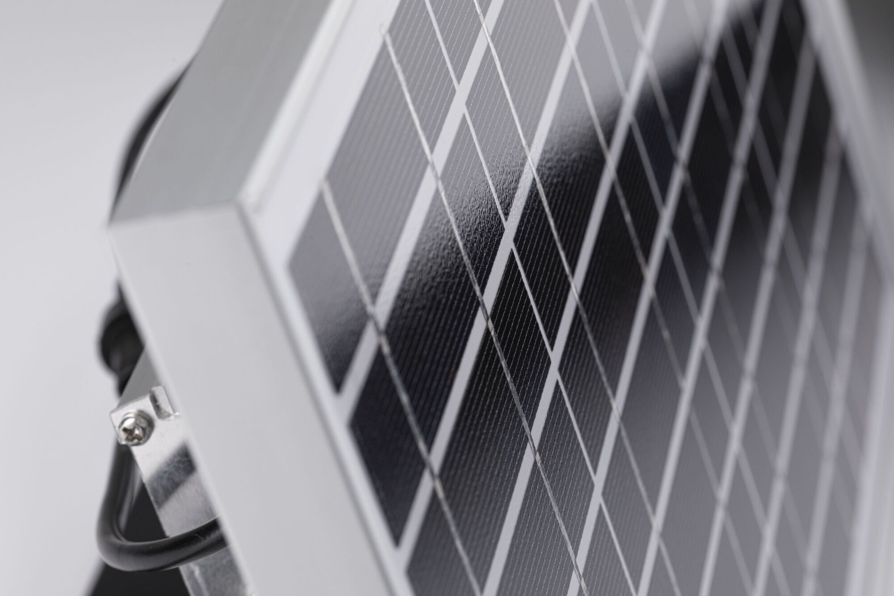 Nahaufnahme eines Solarpanels. Es besteht aus dunklen Quadraten und weißen Linien. Ein Metallrahmen und ein schwarzes Kabel sind ebenfalls sichtbar.