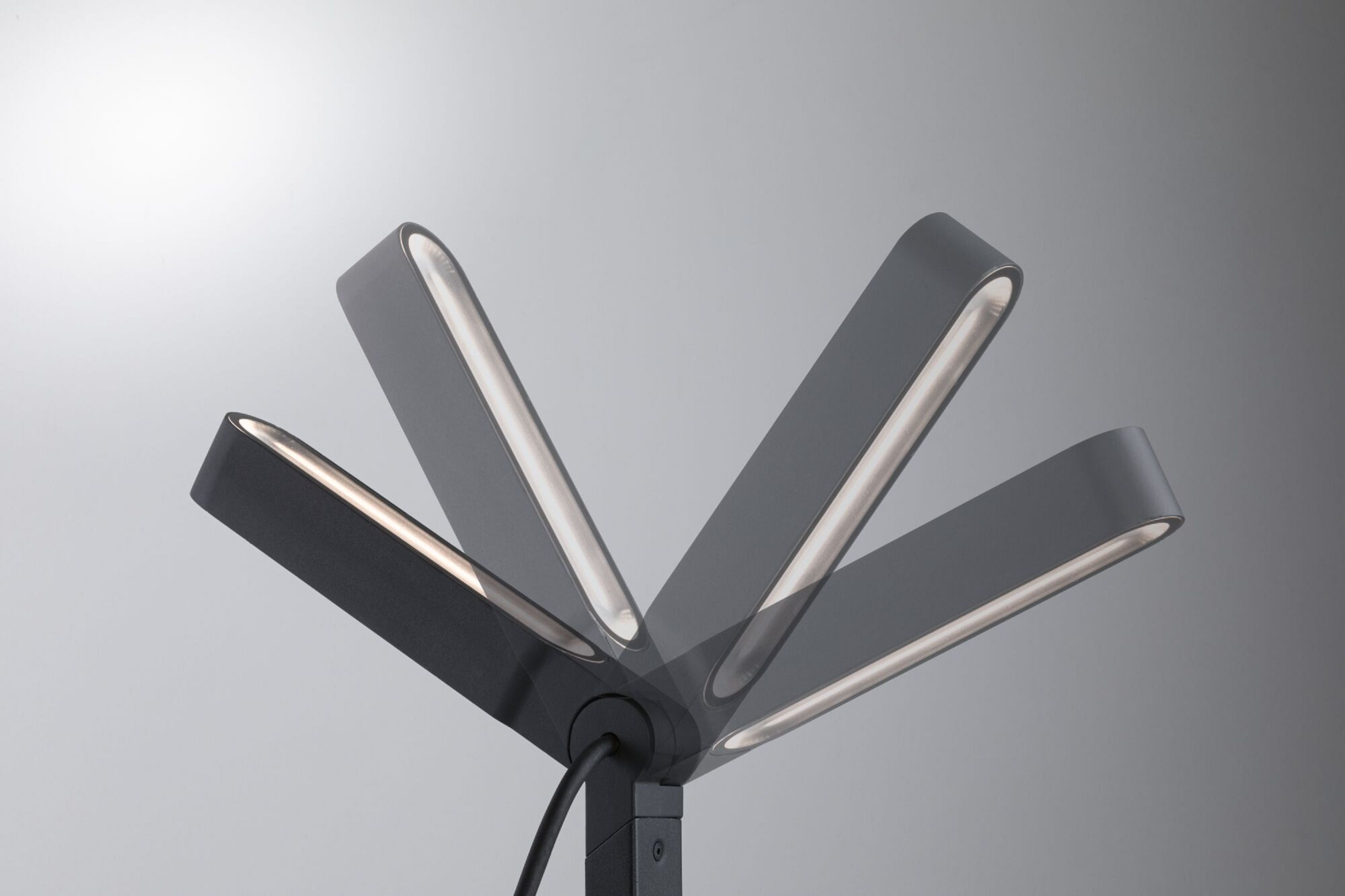 Eine moderne schwarze Lampe mit mehreren schwenkbaren Lichtpaneelen, die ein weiches, weißes Leuchten vor einem grauen Hintergrund erzeugen.