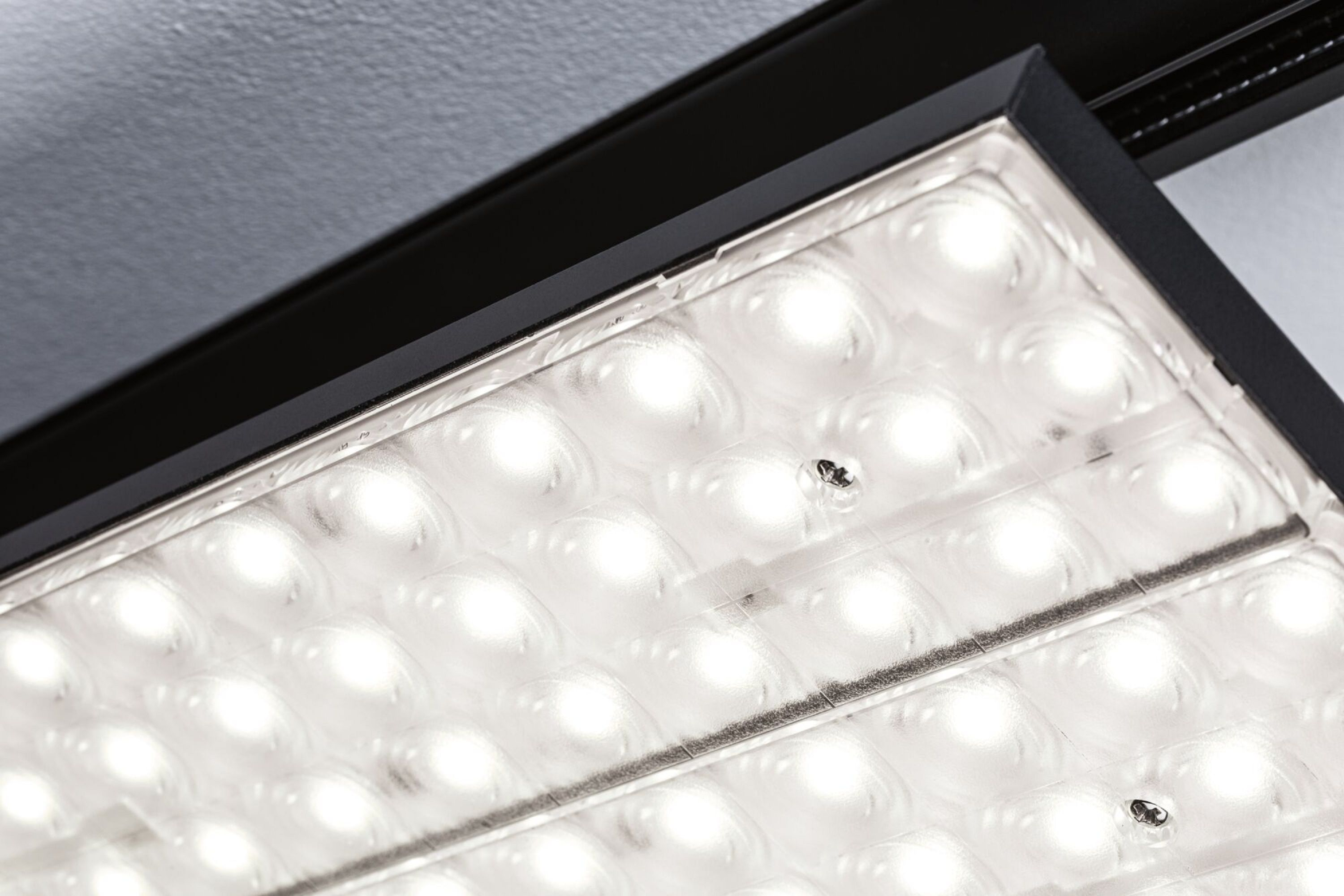 Nahaufnahme einer Deckenleuchte. Sie hat zahlreiche helle, runde Lichter in einem schwarzen Rahmen.
