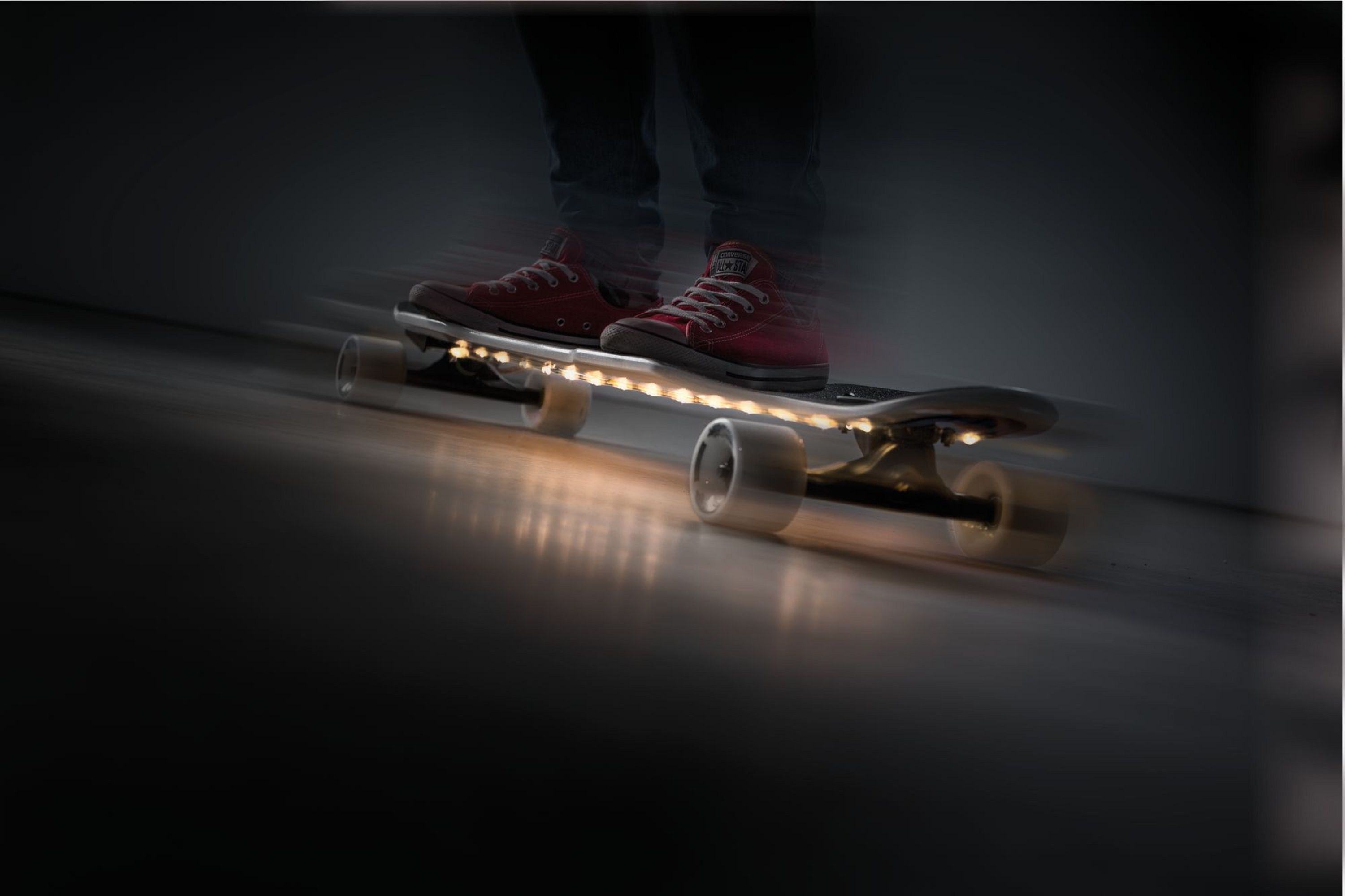 Eine Person auf einem Skateboard mit roten Schuhen in Bewegung. Das Board hat Lichter.