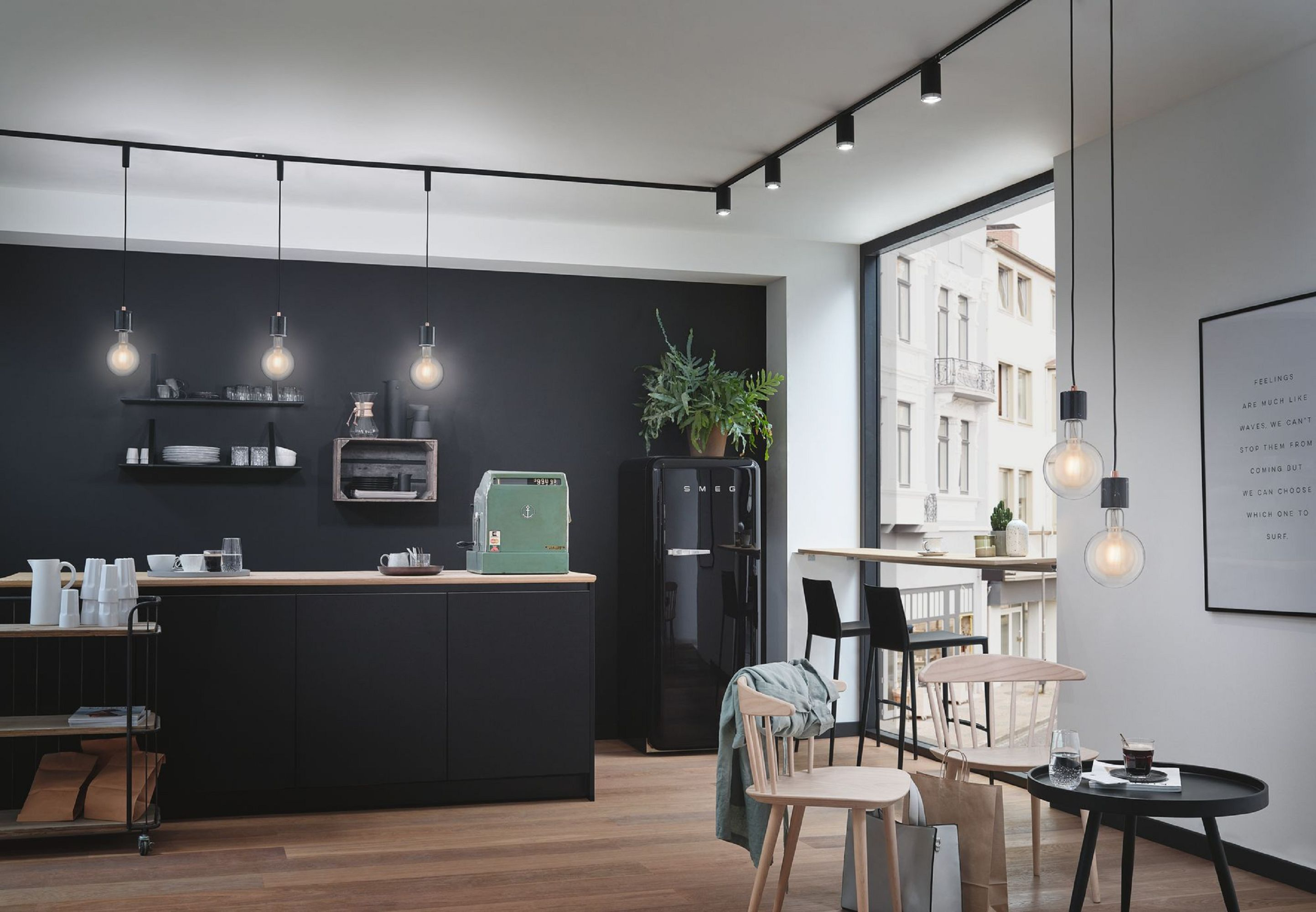 Moderne Küche mit schwarzer Wand, Geräten und Holzboden. Enthält Kühlschrank, Kaffeemaschine und Hängeleuchten.