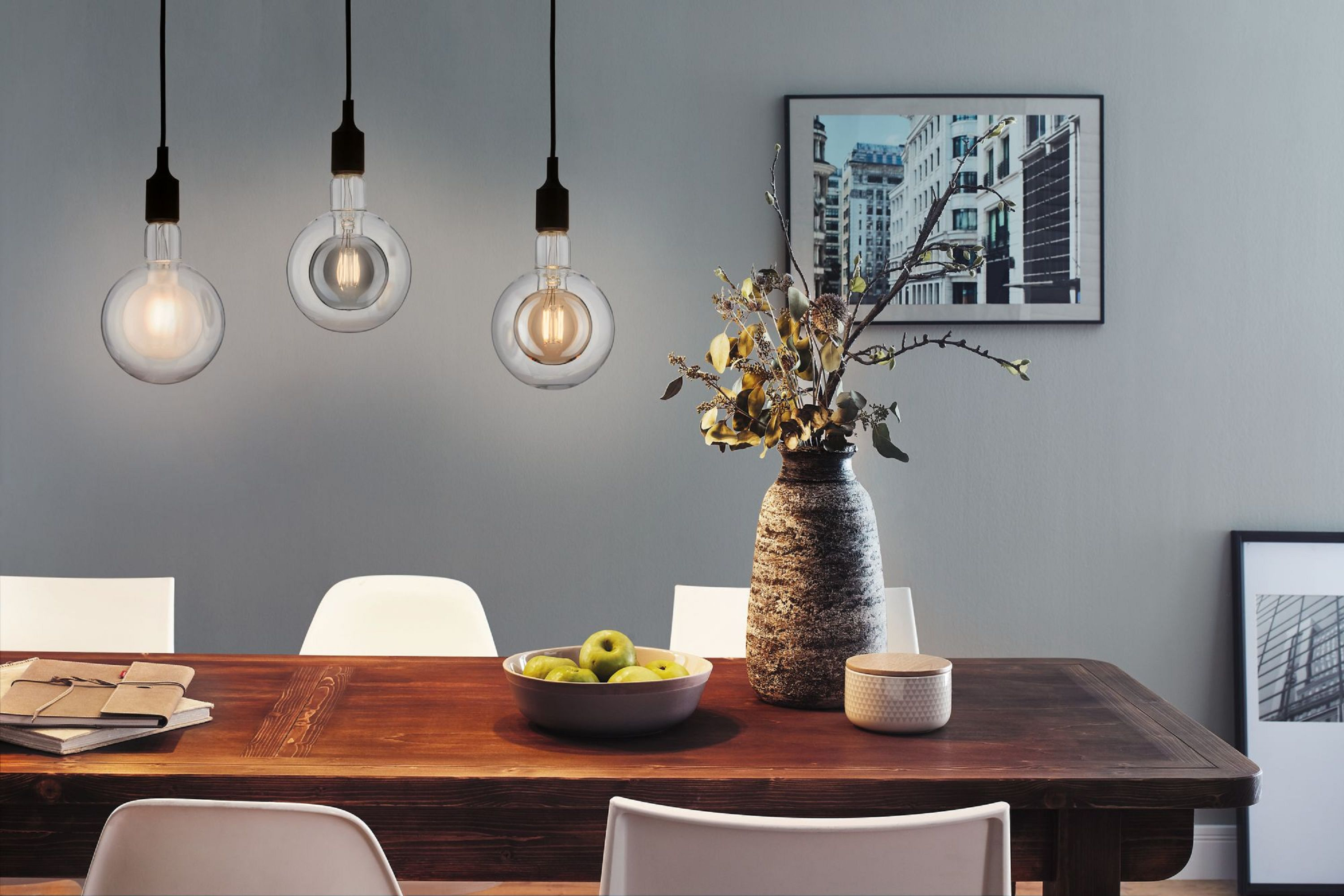 Esszimmer mit Holztisch, Lampen, Vase mit Blumen und Bilderrahmen an der Wand.