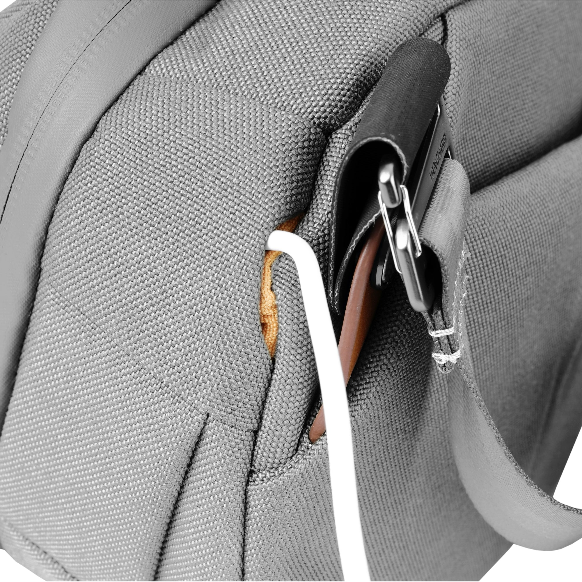 Nahaufnahme eines grauen Rucksacks mit schwarzem Riemen, Metallclips und einem weißen Kabel. In der Tasche befindet sich ein brauner Lederartikel.
