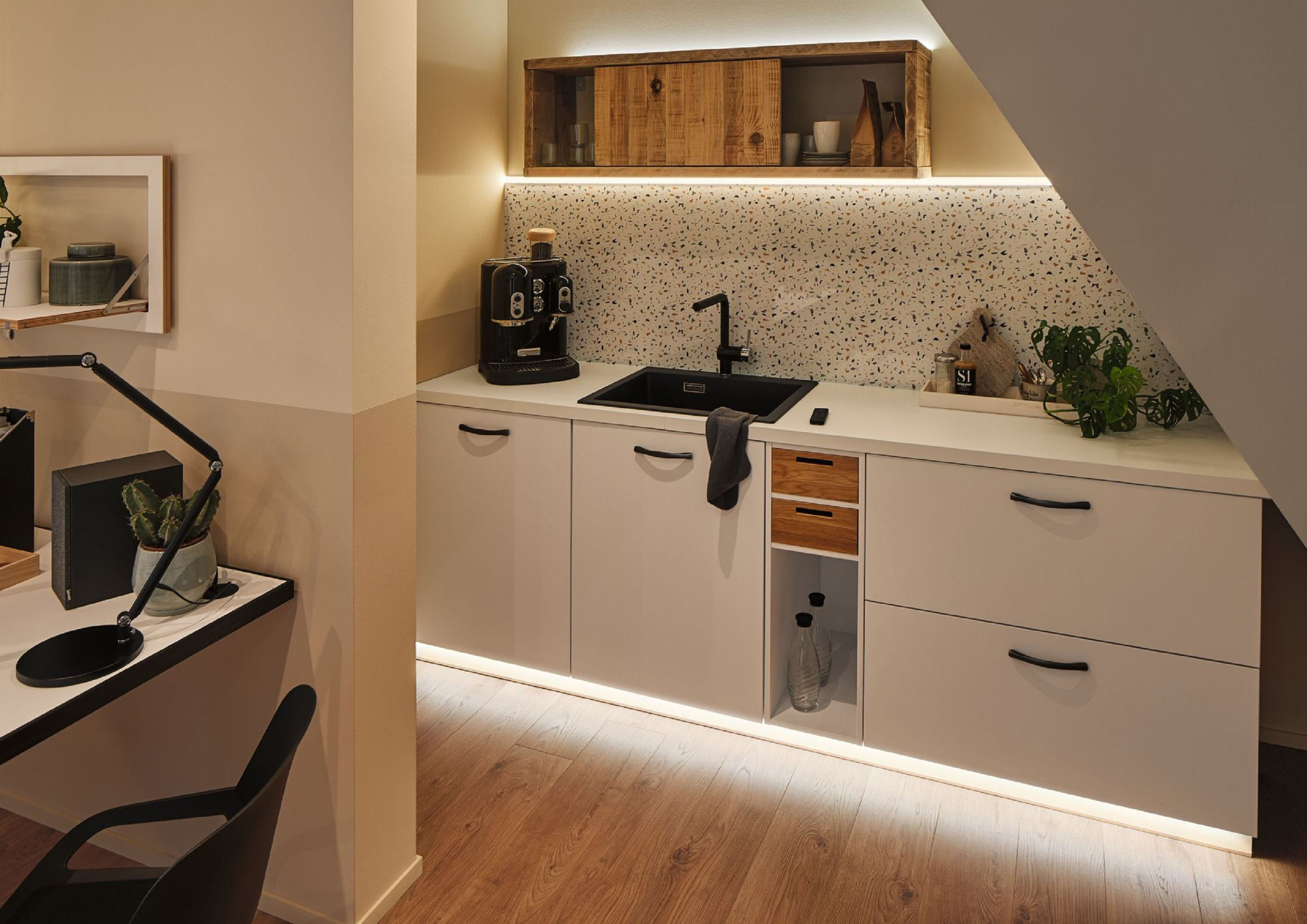 Moderne Küche mit weißen Schränken, schwarzem Wasserhahn, Espressomaschine und Holzakzenten. Mit Schreibtischbereich.