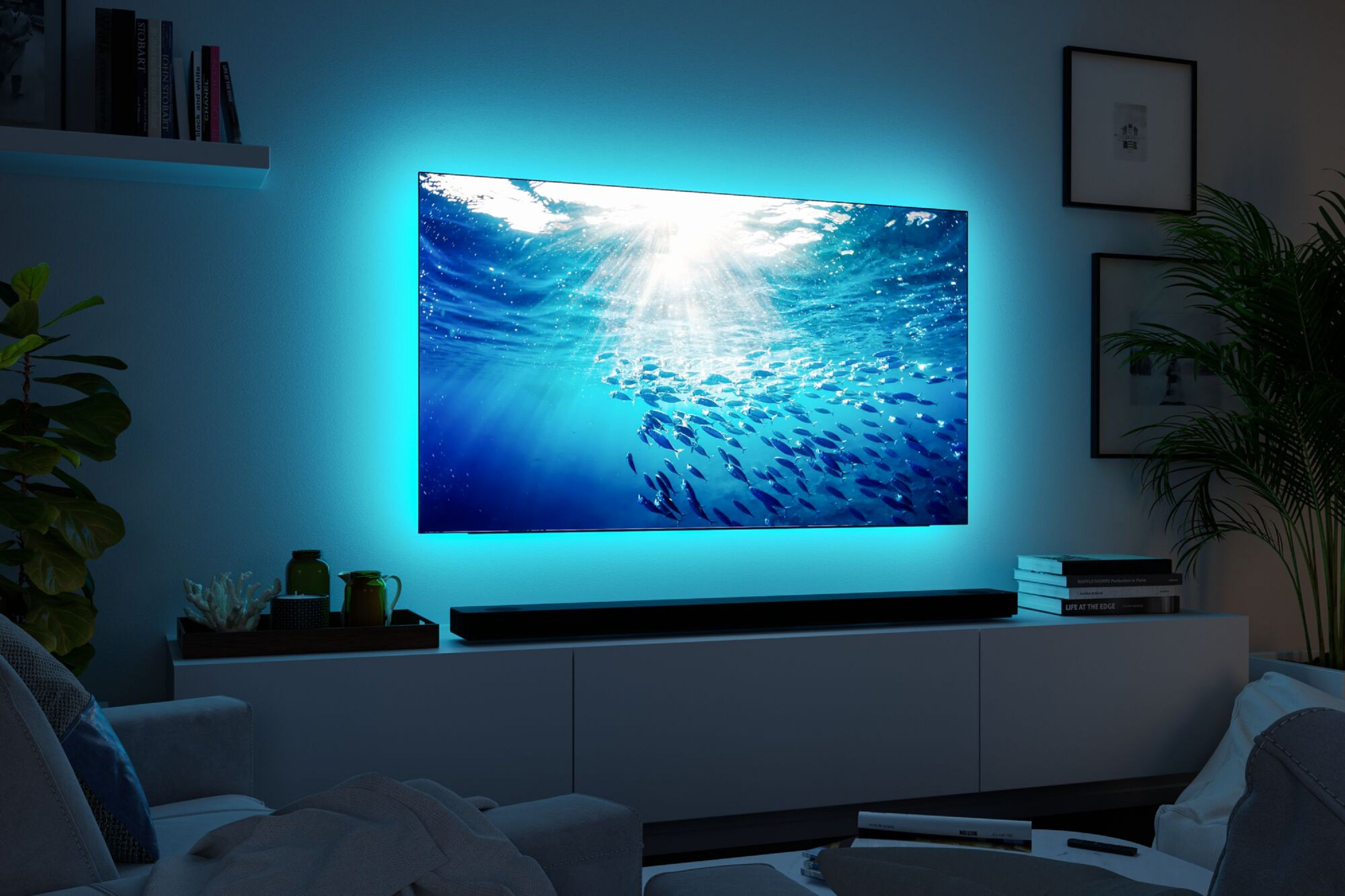 Ein Fernseher zeigt eine Unterwasserszene mit Fischen. Blaues Umgebungslicht umgibt ihn. Im Raum befinden sich eine Soundbar und ein Sofa.