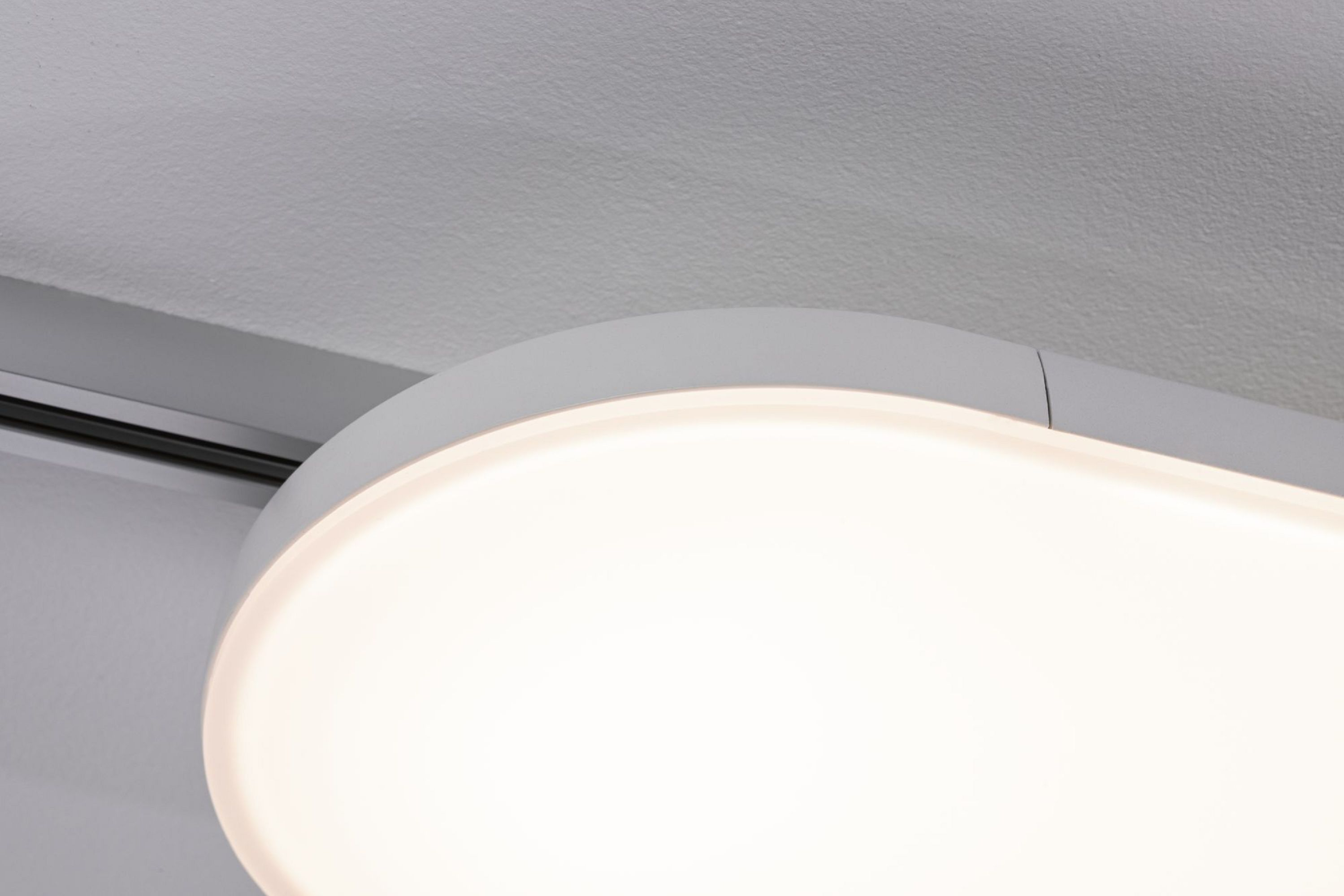 Nahaufnahme einer weißen, länglichen Deckenleuchte. Das Licht ist an und strahlt warm. Die Decke ist weiß.