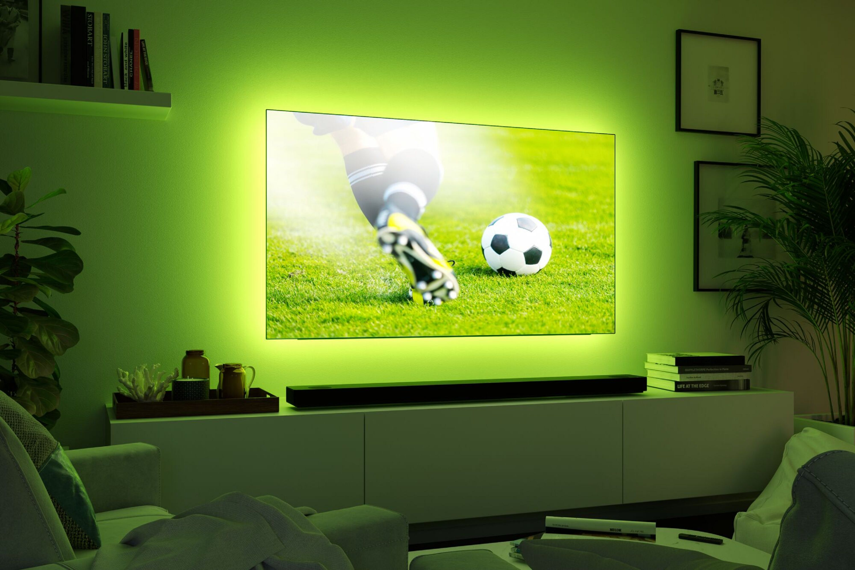 Un televisore mostra una partita di calcio. Un giocatore calcia la palla sull'erba verde. La stanza ha un'illuminazione ambientale verde.