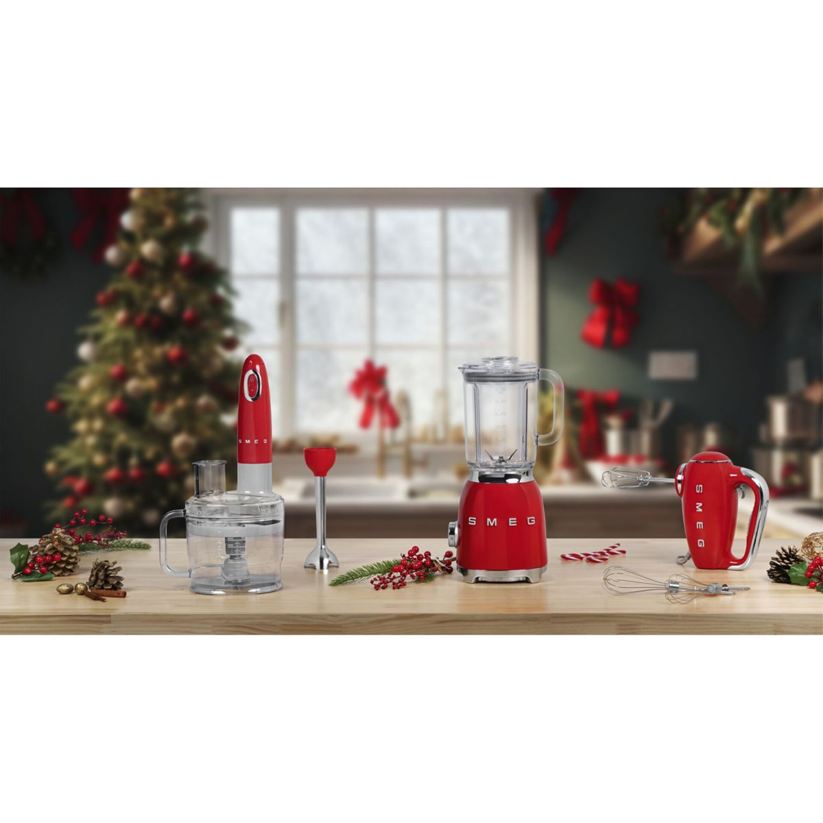 Scena kuchenna z czerwonymi urządzeniami SMEG: blender, mikser i robot kuchenny. Choinka i dekoracje w tle.