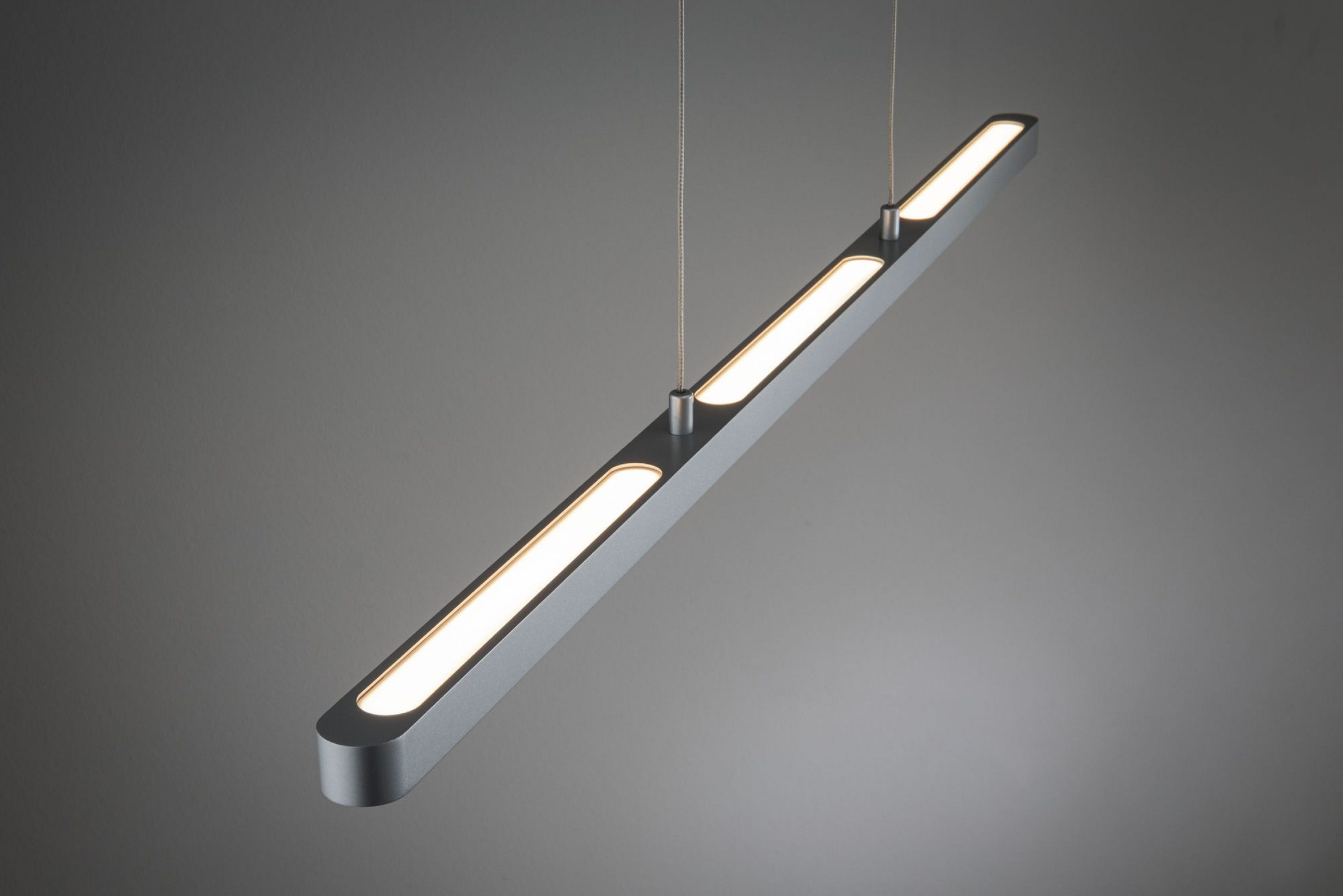 Un moderno apparecchio a LED argentato è appeso a fili sottili. Ha tre sezioni illuminate su sfondo grigio.