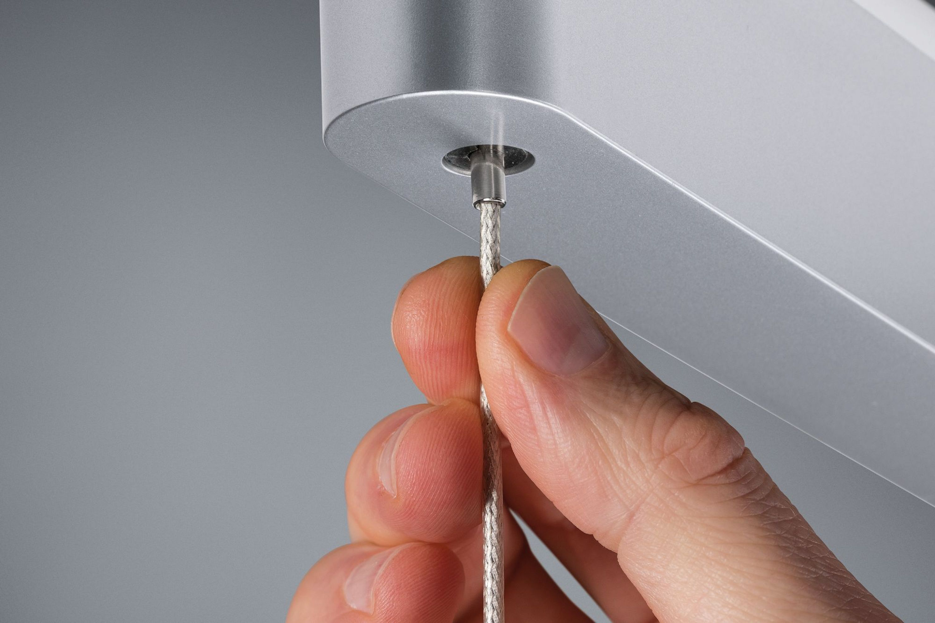 Una mano tiene un cavo d'argento collegato a un dispositivo metallico su sfondo grigio.