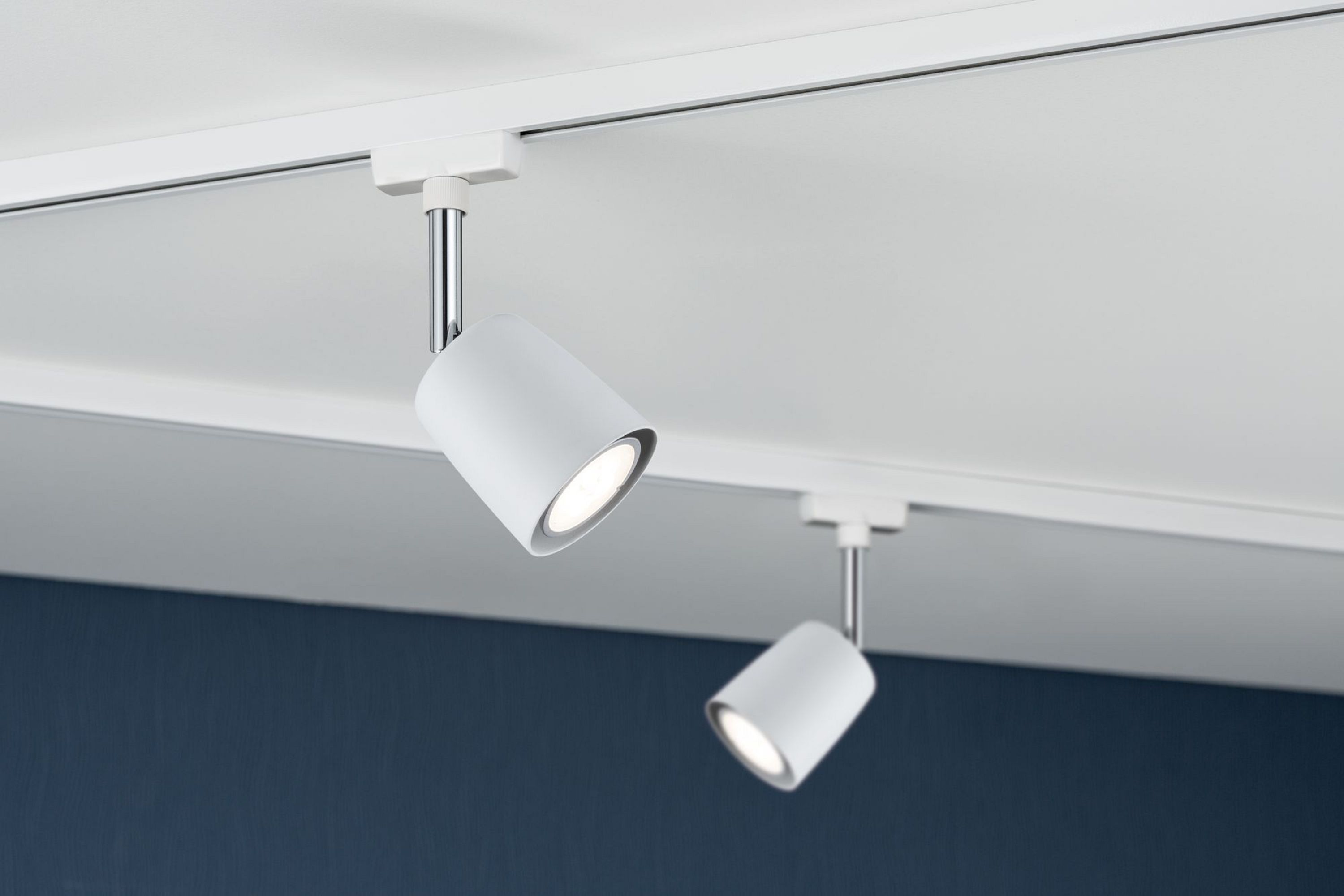 Faretti bianchi su un soffitto bianco. Uno è angolato verso il basso, l'altro verso destra. Parete blu sullo sfondo.