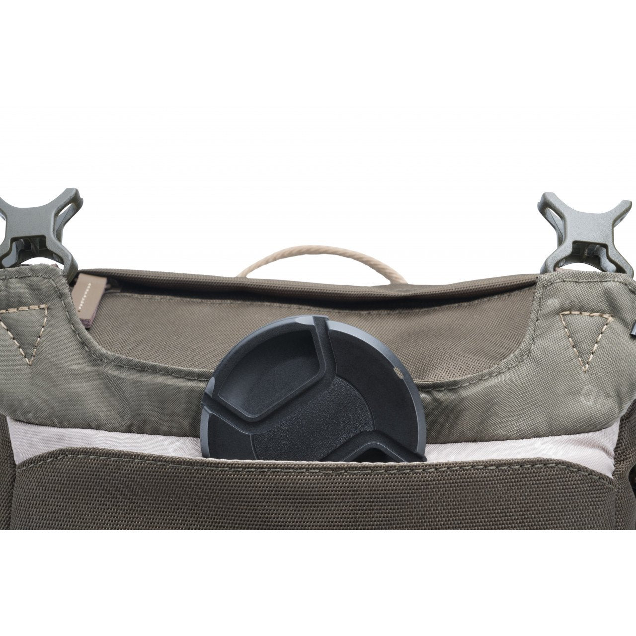 Primer plano de una bolsa de cámara. Una tapa negra de lente está en un bolsillo. La bolsa es verde oliva con clips grises y un asa beige.