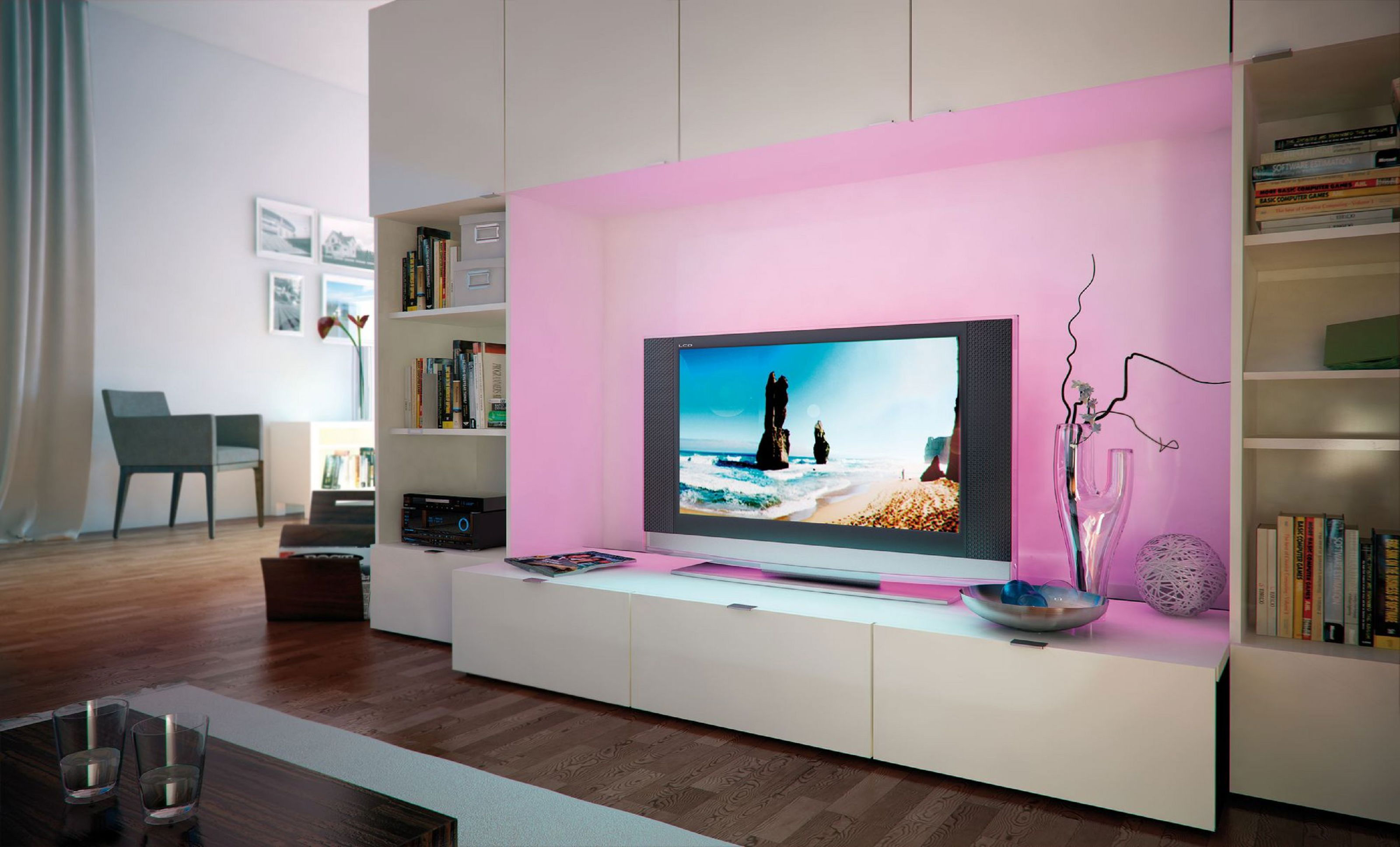 Soggiorno con TV che mostra una scena di spiaggia, mobili bianchi e librerie. Due sedie e un tavolo con bicchieri in primo piano.