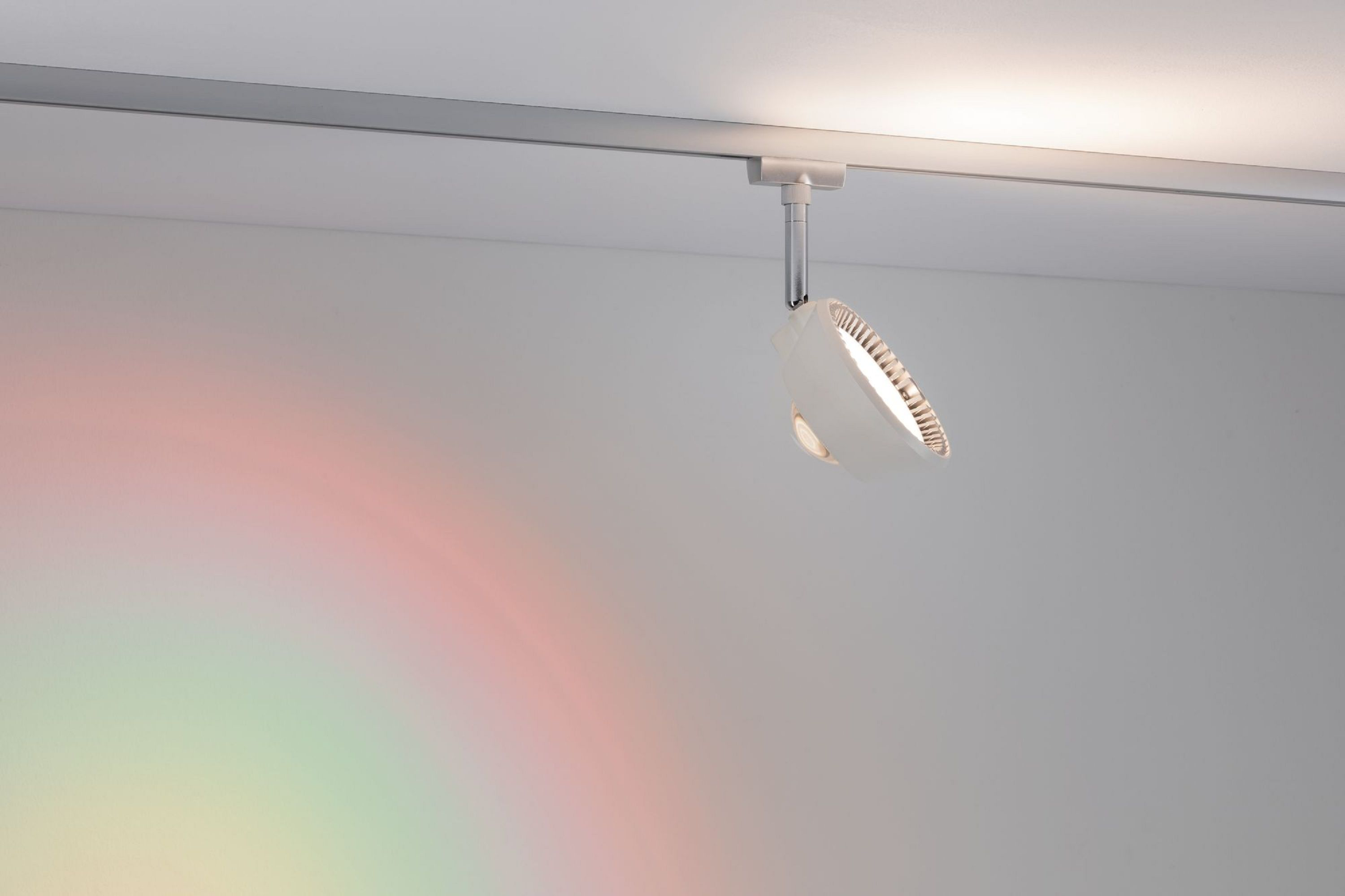 Ein weißer Strahler auf einer Schiene, der Licht projiziert. Ein regenbogenartiges Spektrum erscheint an der Wand.