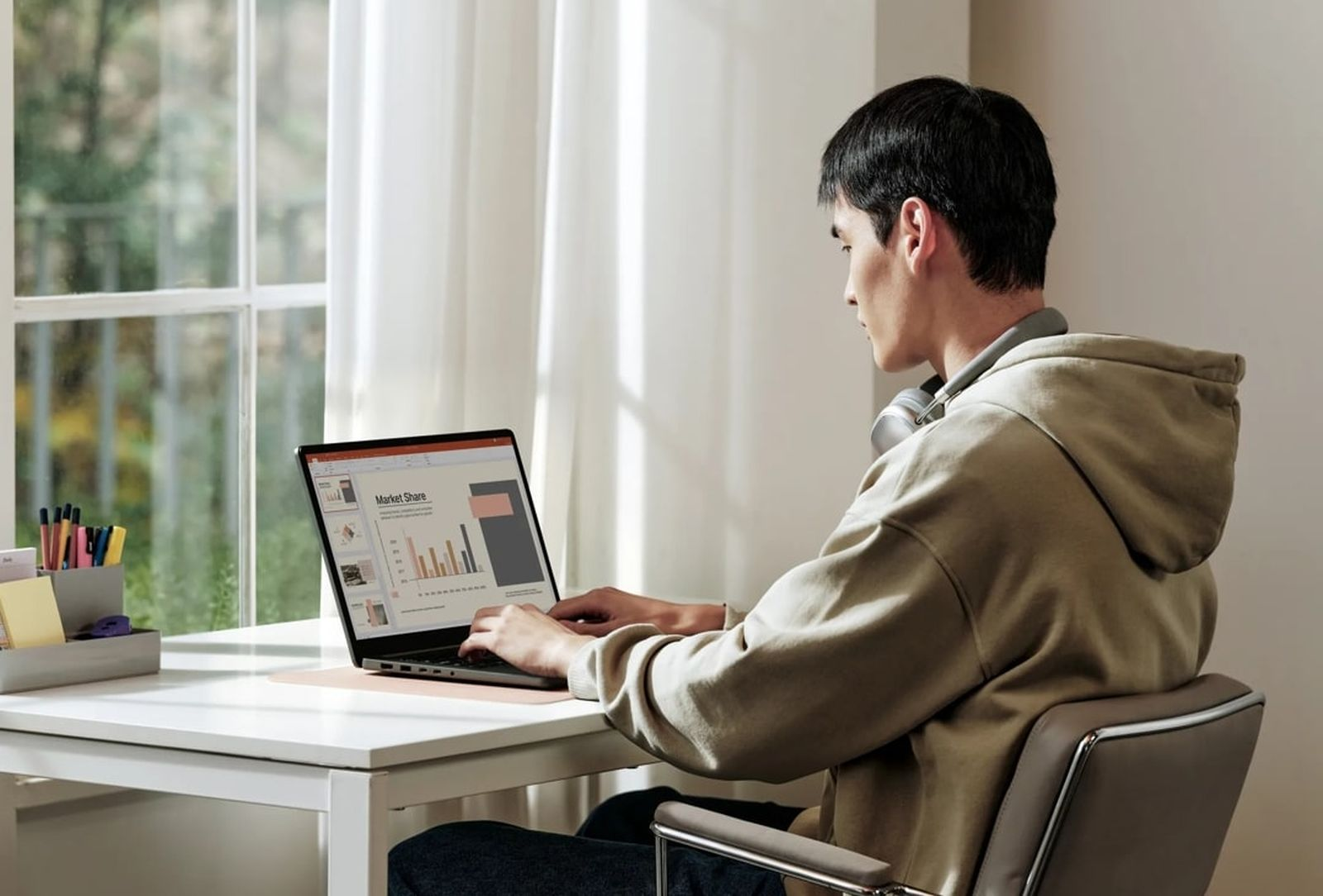 Osoba siedzi przy biurku i używa laptopa. W tle widać okno. Na ekranie prezentacja udziału w rynku.