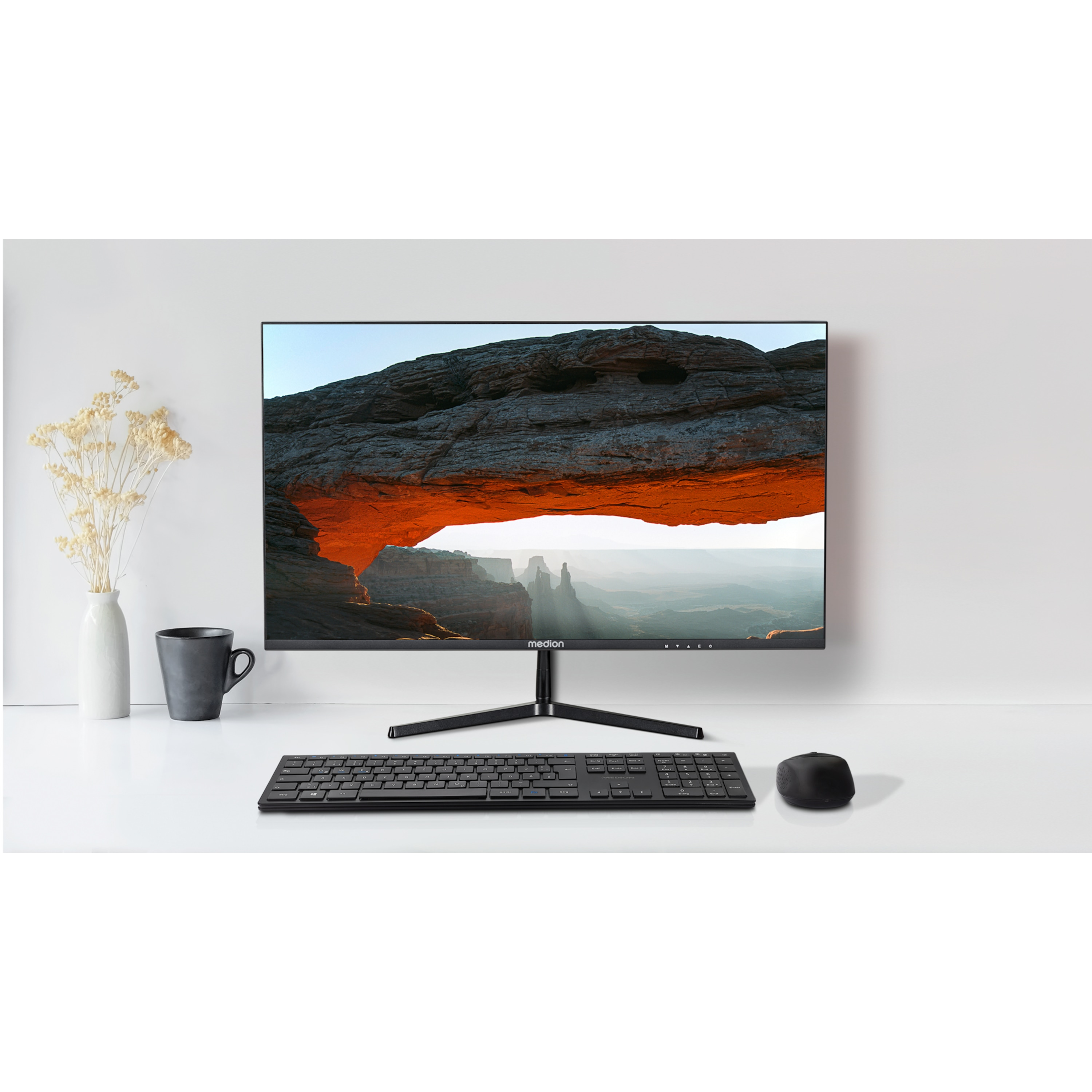 Een computermonitor toont een landschap. Het staat op een witte bureau met toetsenbord, muis, mok en vaas.