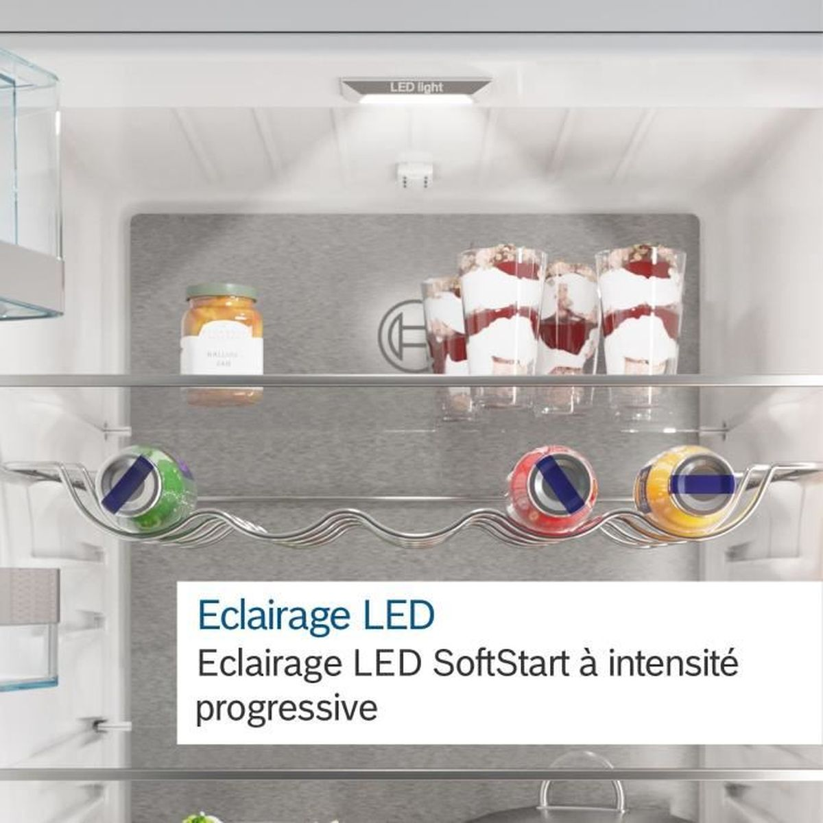 Dentro de la nevera: tarro de mermelada, postres en vasos y bebidas enlatadas. La luz LED ilumina el contenido.