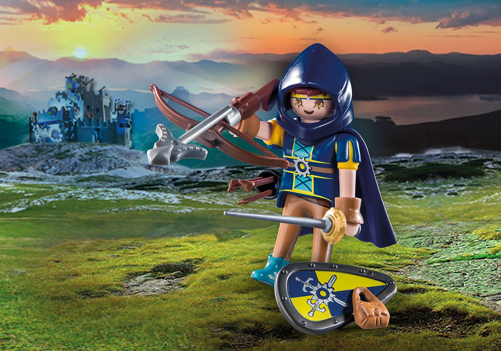 Figurka Playmobil w niebiesko-żółtym średniowiecznym stroju trzyma kuszę. Na tle zamek, na tle zachodu słońca.