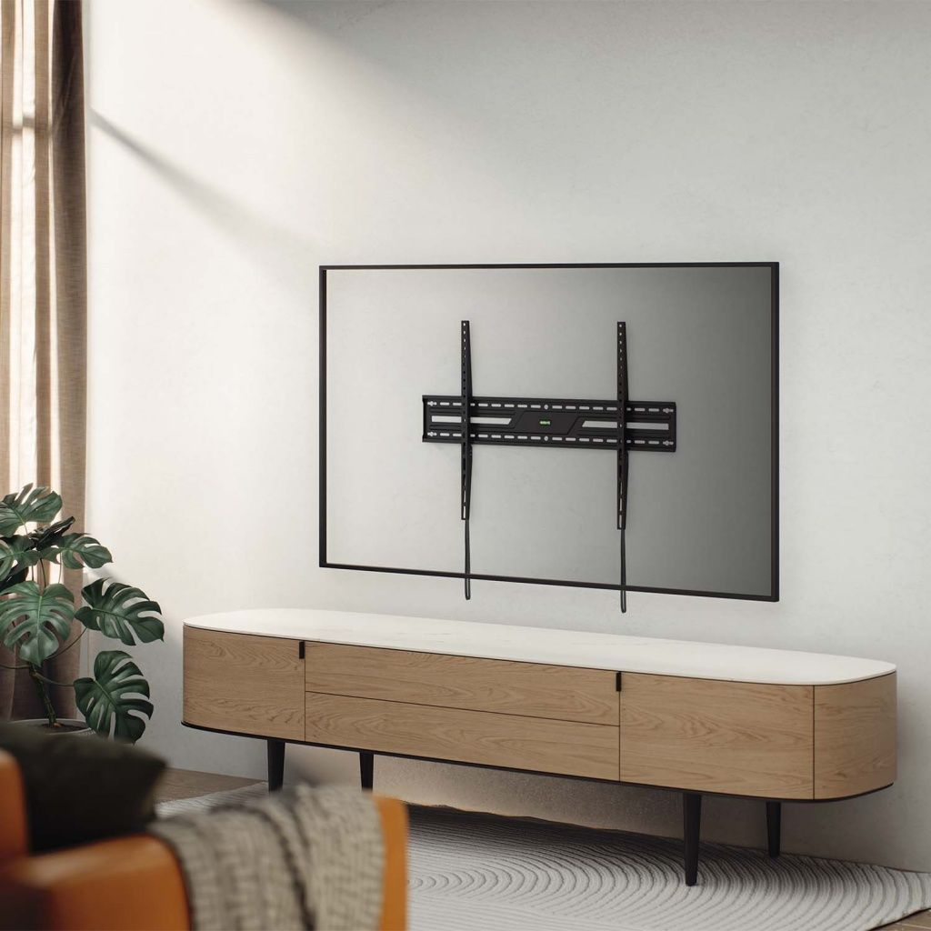 Un soporte de TV en una pared blanca. Un mueble de madera debajo. Una planta y una ventana con cortinas a la izquierda.